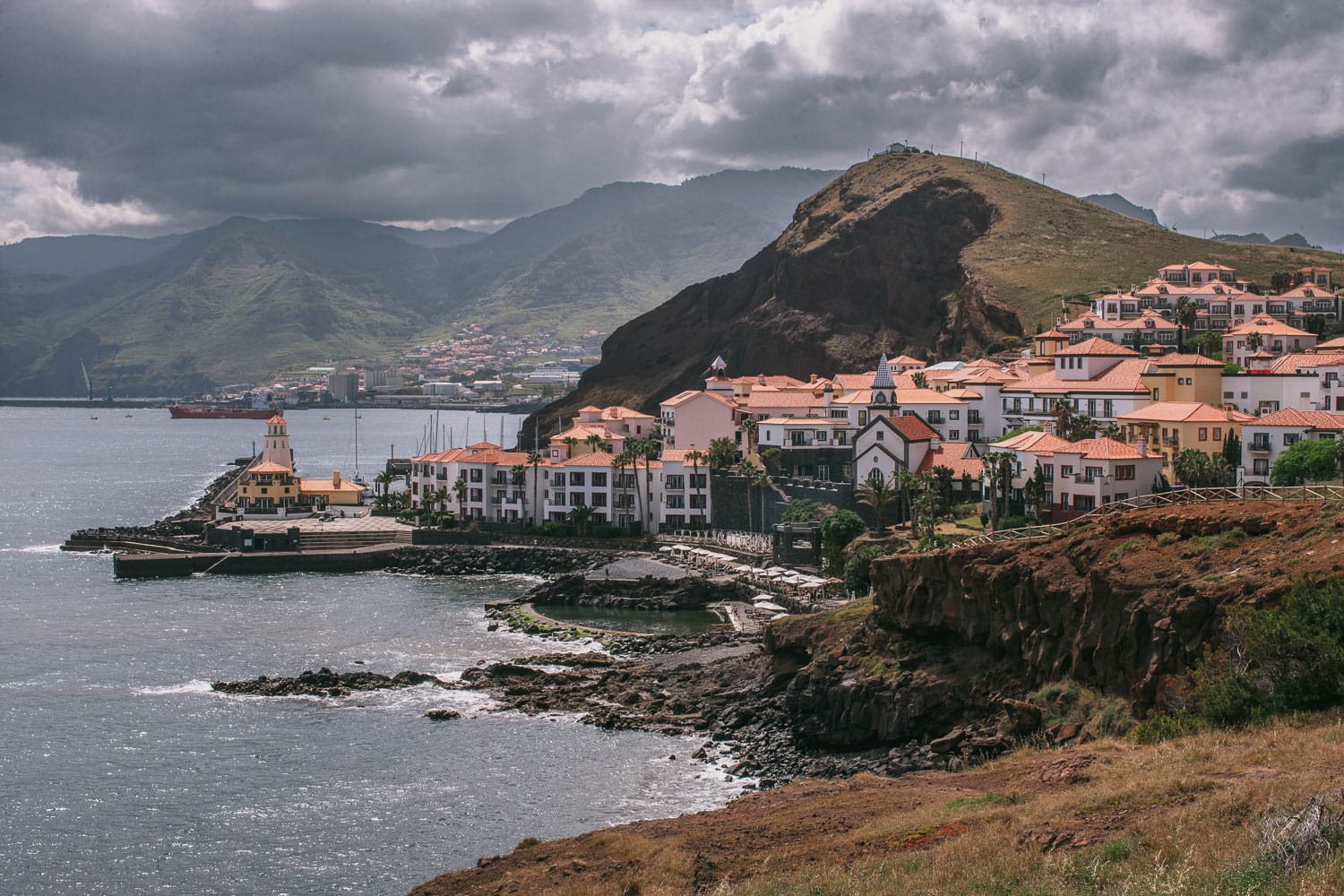 Quinta do Lorde marina village seen from miradouro viewpoint, red-tile roofs, lighthouse, mountain backdrop, eastern Madeira