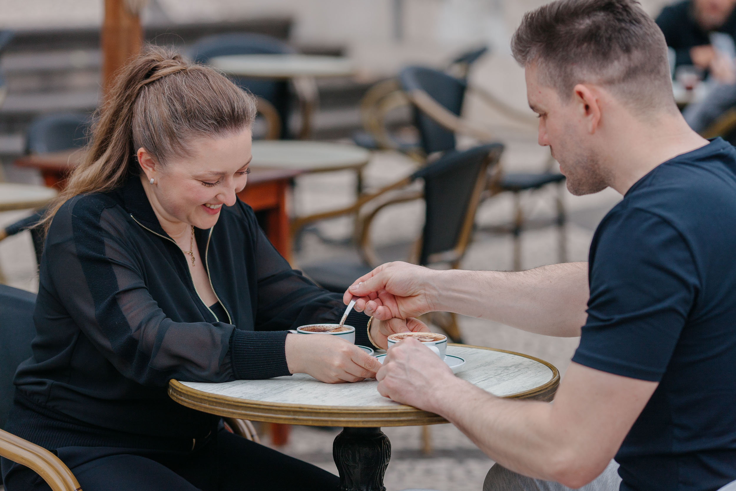 Both laughing at a cafe table, she holding a spoon mid-gesture, natural candid moment, Funchal, Madeira