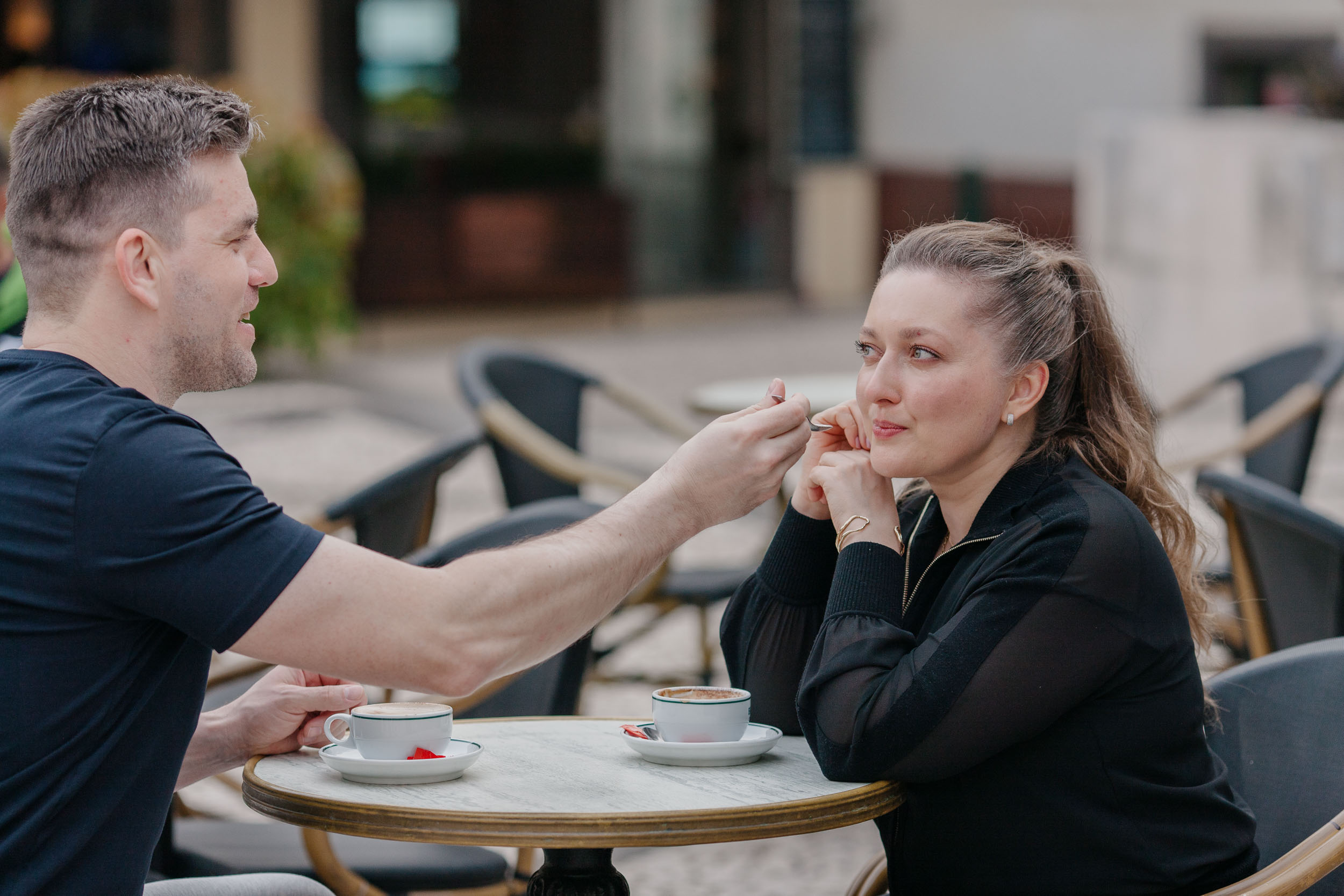Man feeding woman at a cafe table, she looking up at him, intimate and playful, Funchal, Madeira
