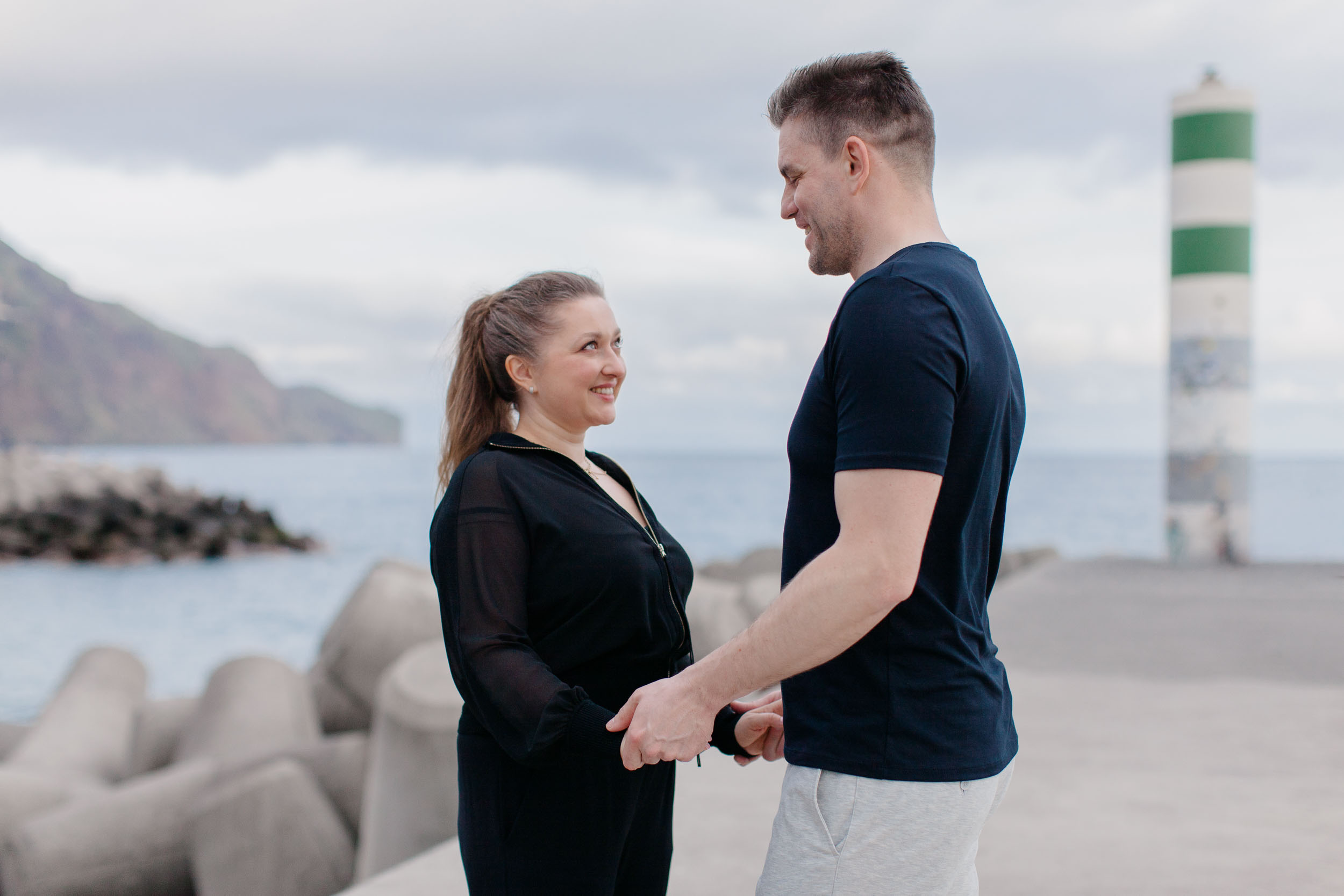 Couple face to face at Funchal lighthouse, dramatic Atlantic cliffs and sky behind them, Madeira