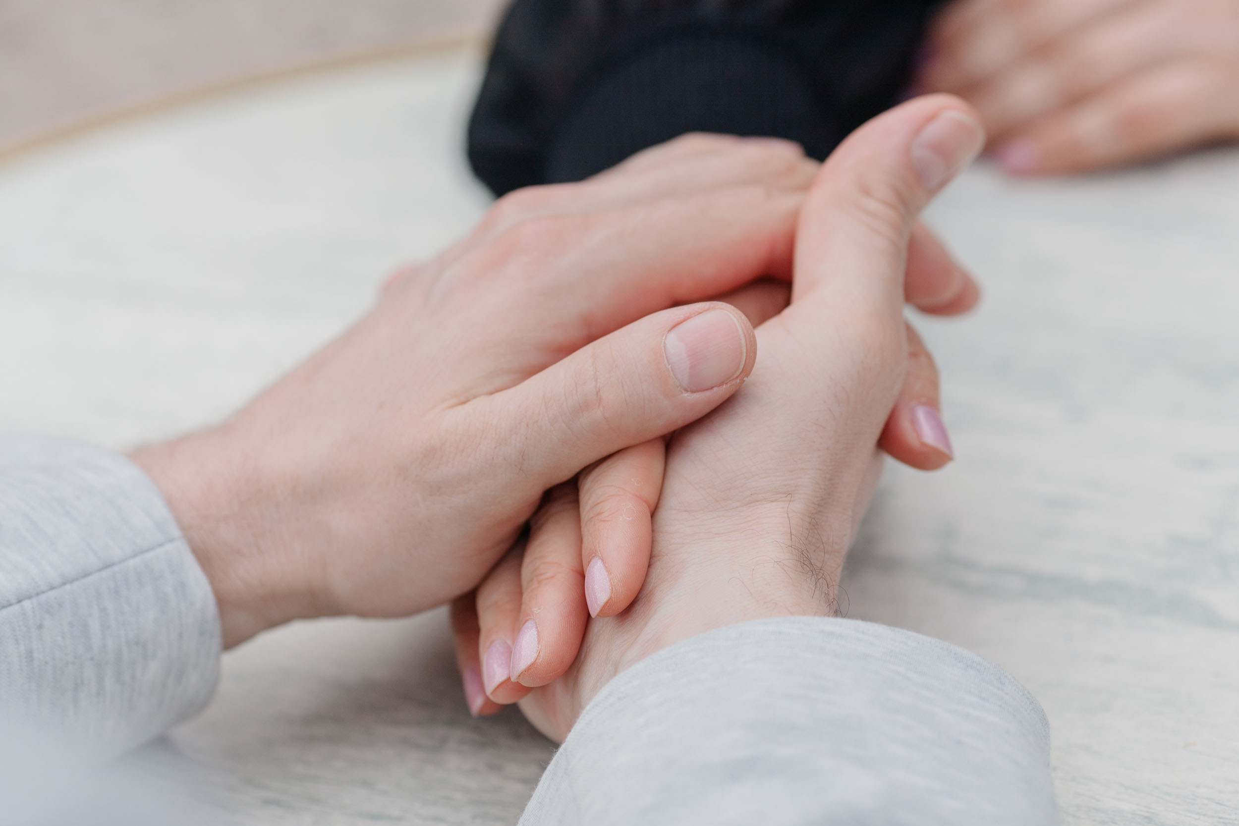 Close-up of couple's hands intertwined on a cafe table, two coffee cups visible, Funchal, Madeira
