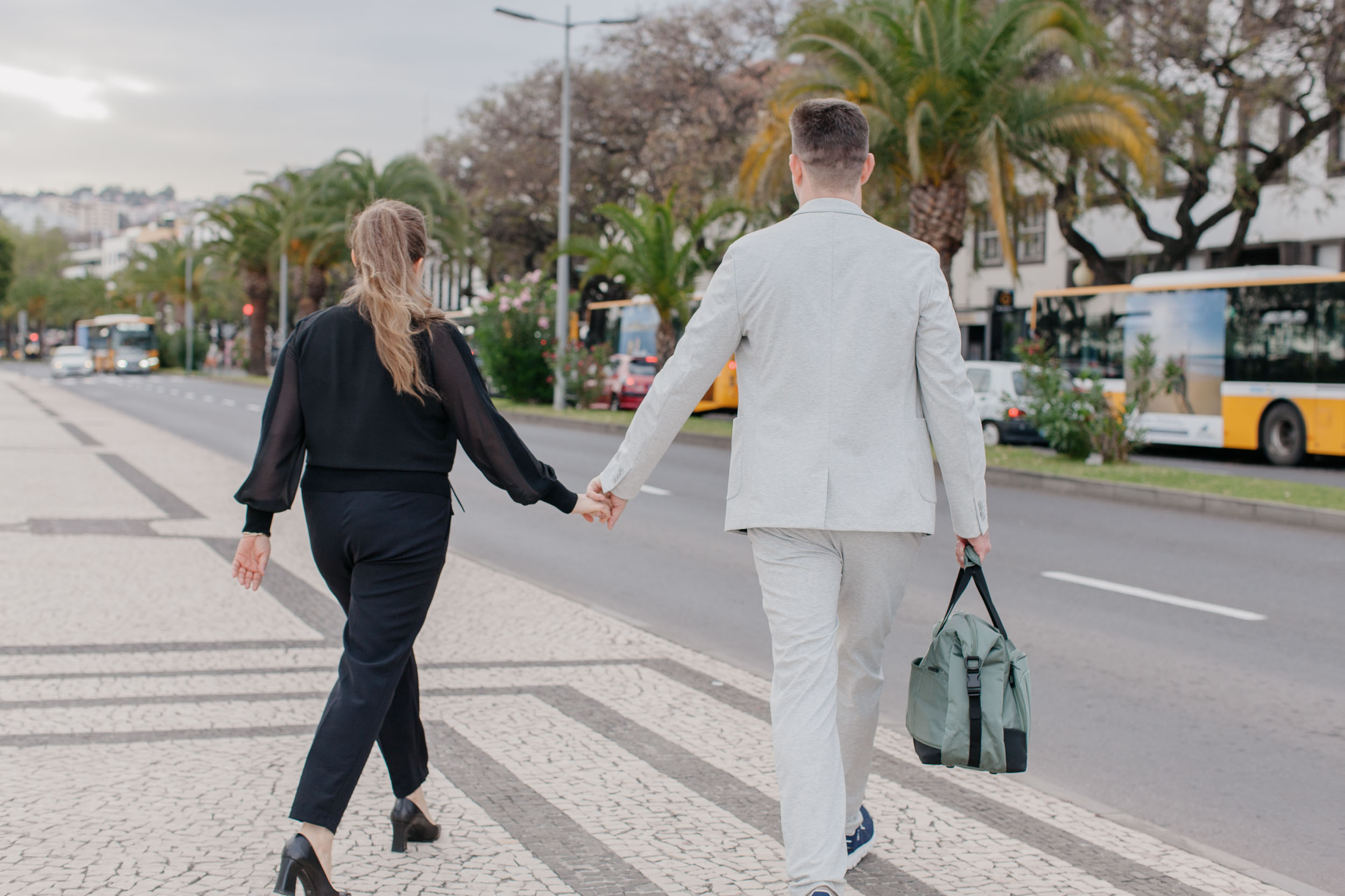 Couple walking along Funchal promenade, city bus behind them, urban atmosphere, Madeira