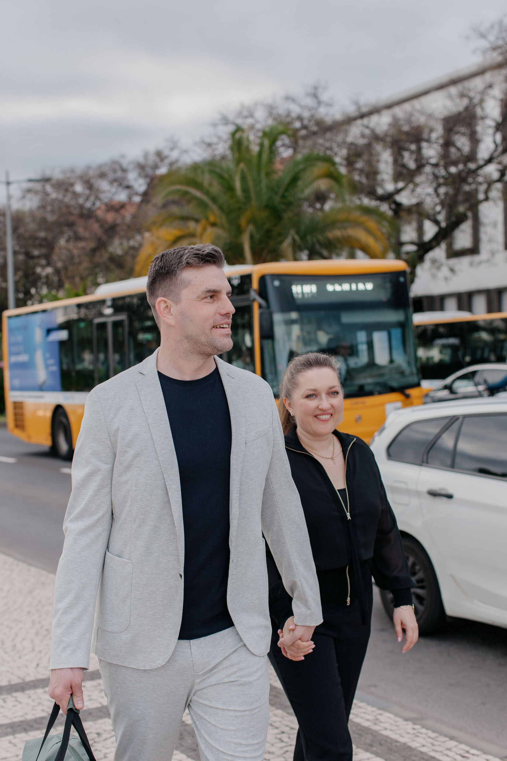 Couple walking along Funchal waterfront promenade, harbor and city buildings behind, Madeira