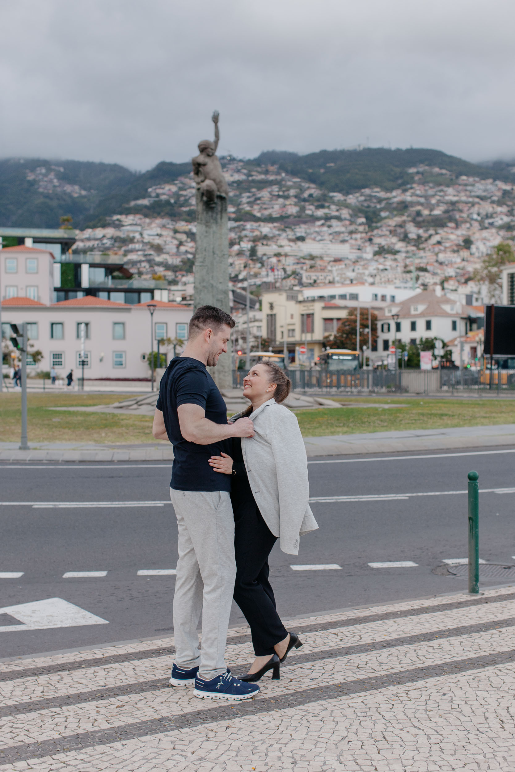 Couple embracing on Funchal waterfront, harbor and city visible behind them, Madeira