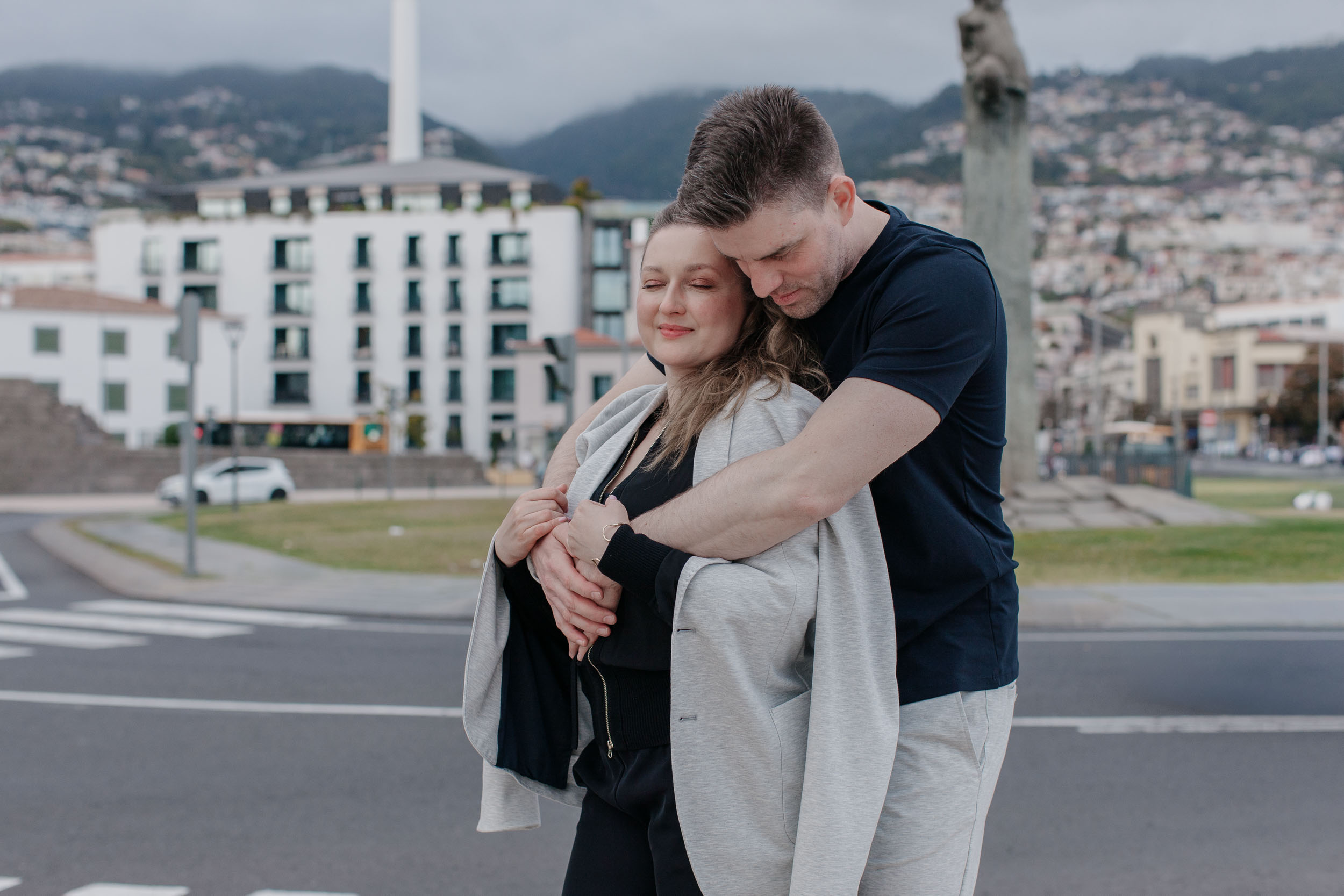 Couple embracing on Funchal waterfront, Funchal skyline and mountains behind, Madeira