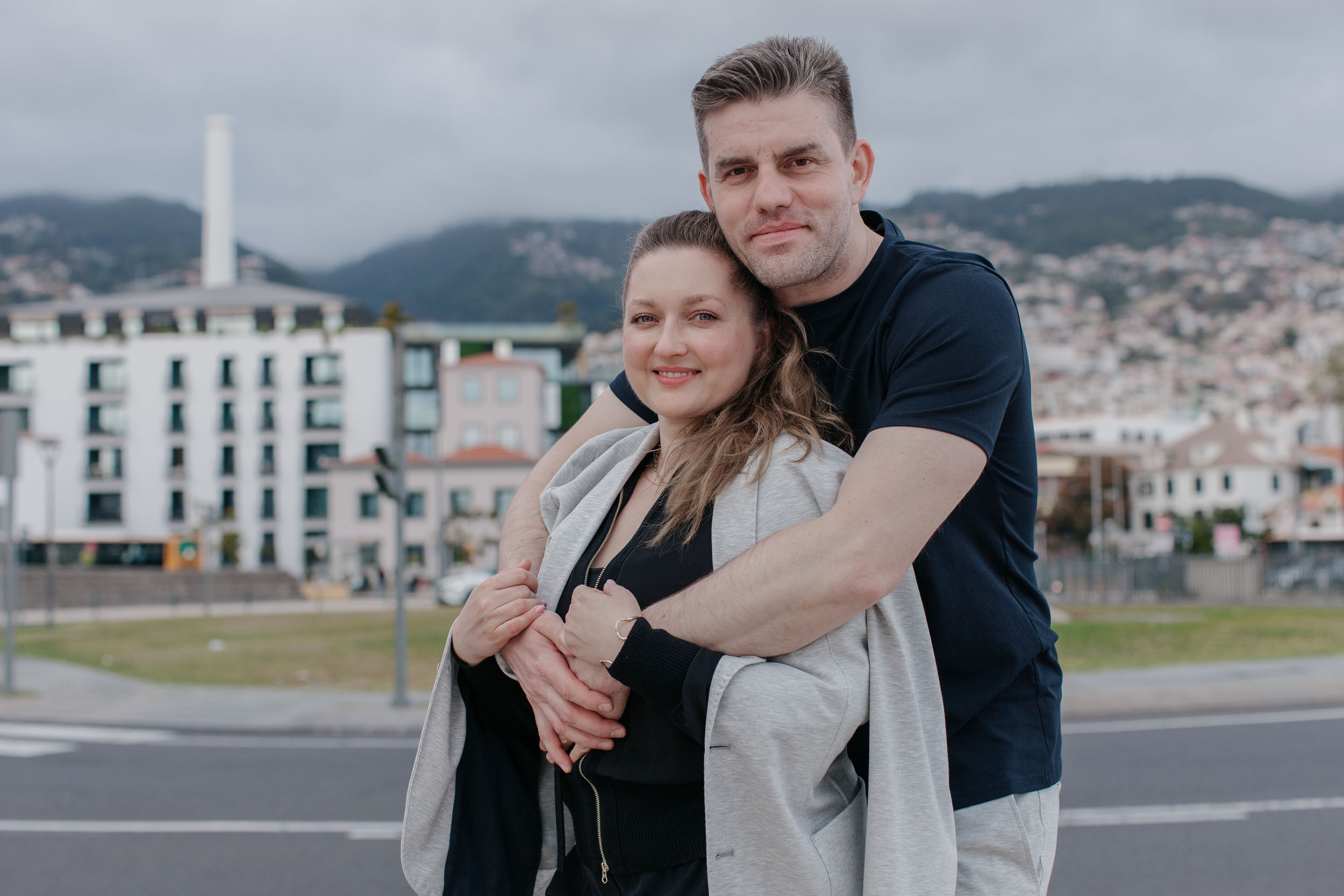 Couple close together on Funchal waterfront, city panorama and mountains behind, Madeira