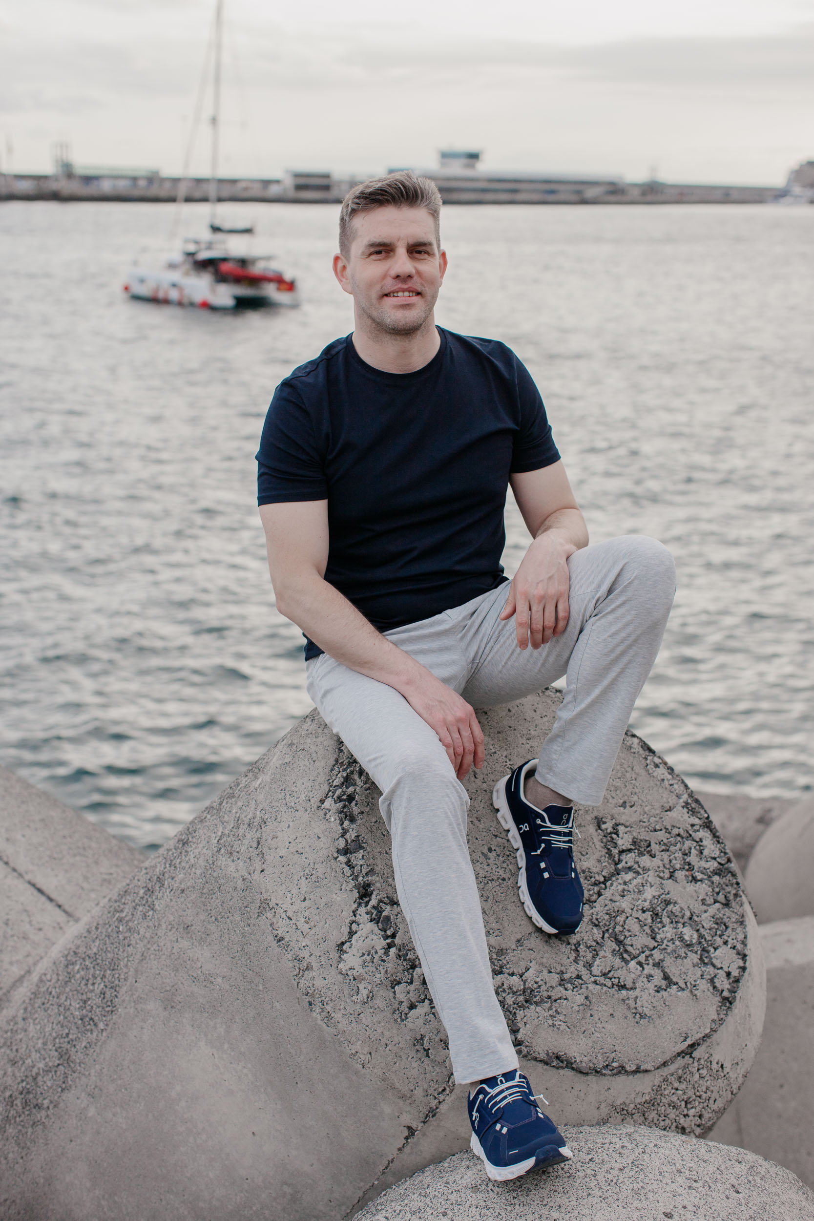 Man sitting on a large coastal rock at Funchal harbor, breakwater and sea behind, Madeira