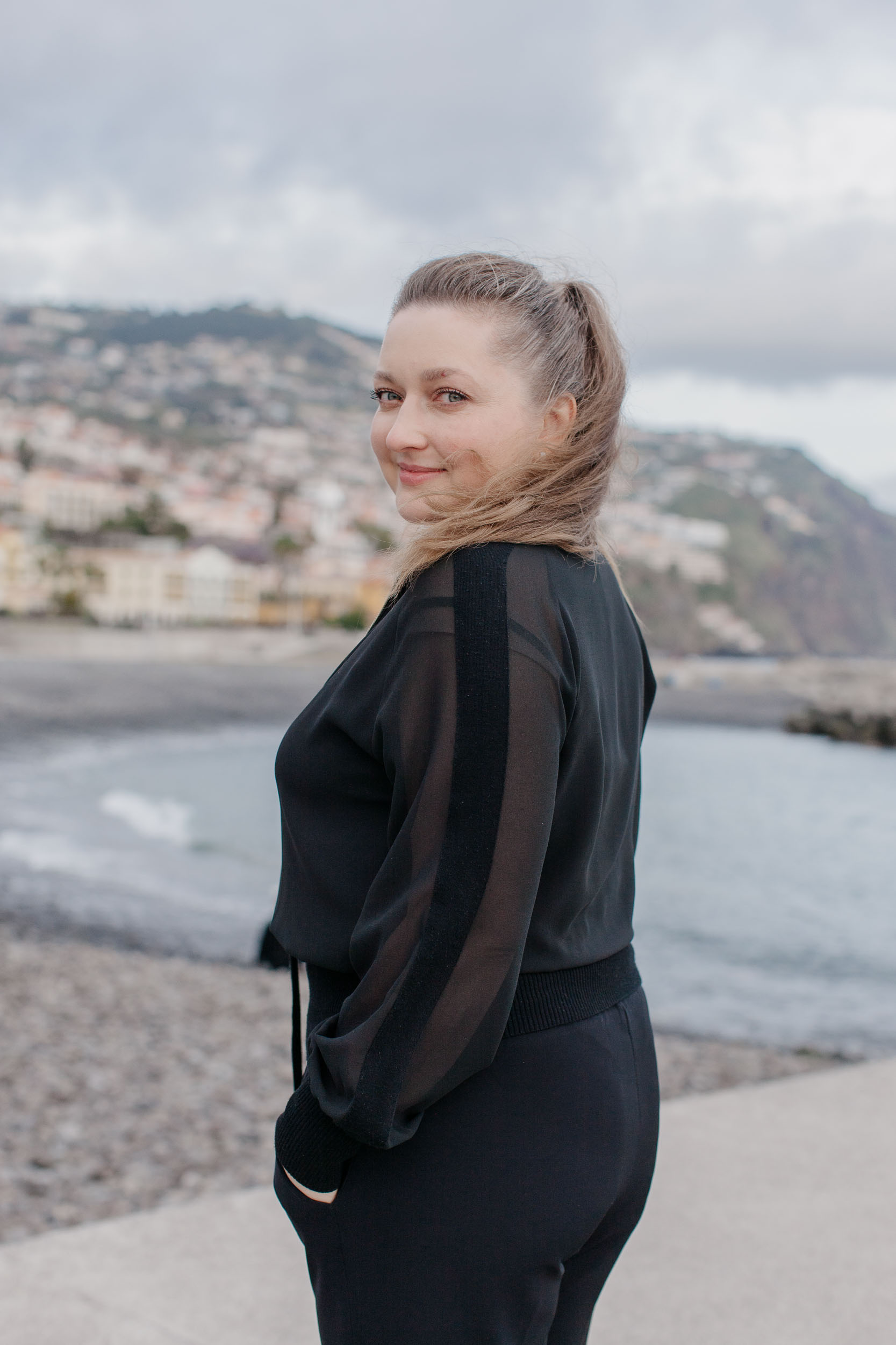 Woman on Funchal pier walkway looking back over her shoulder, harbor and city behind, Madeira