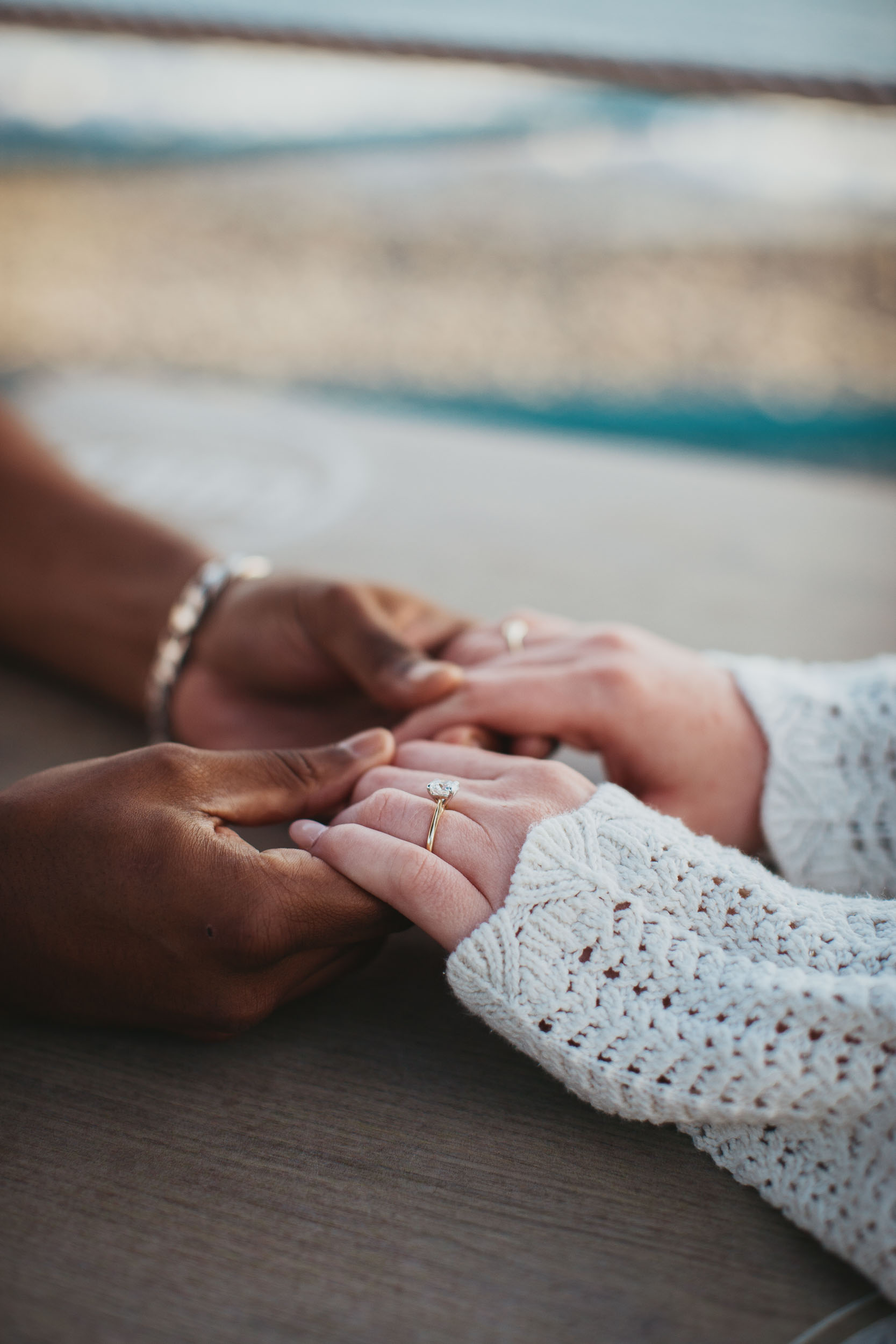 Engagement ring on woman's hand, couple holding hands at Praia Formosa beach, Madeira