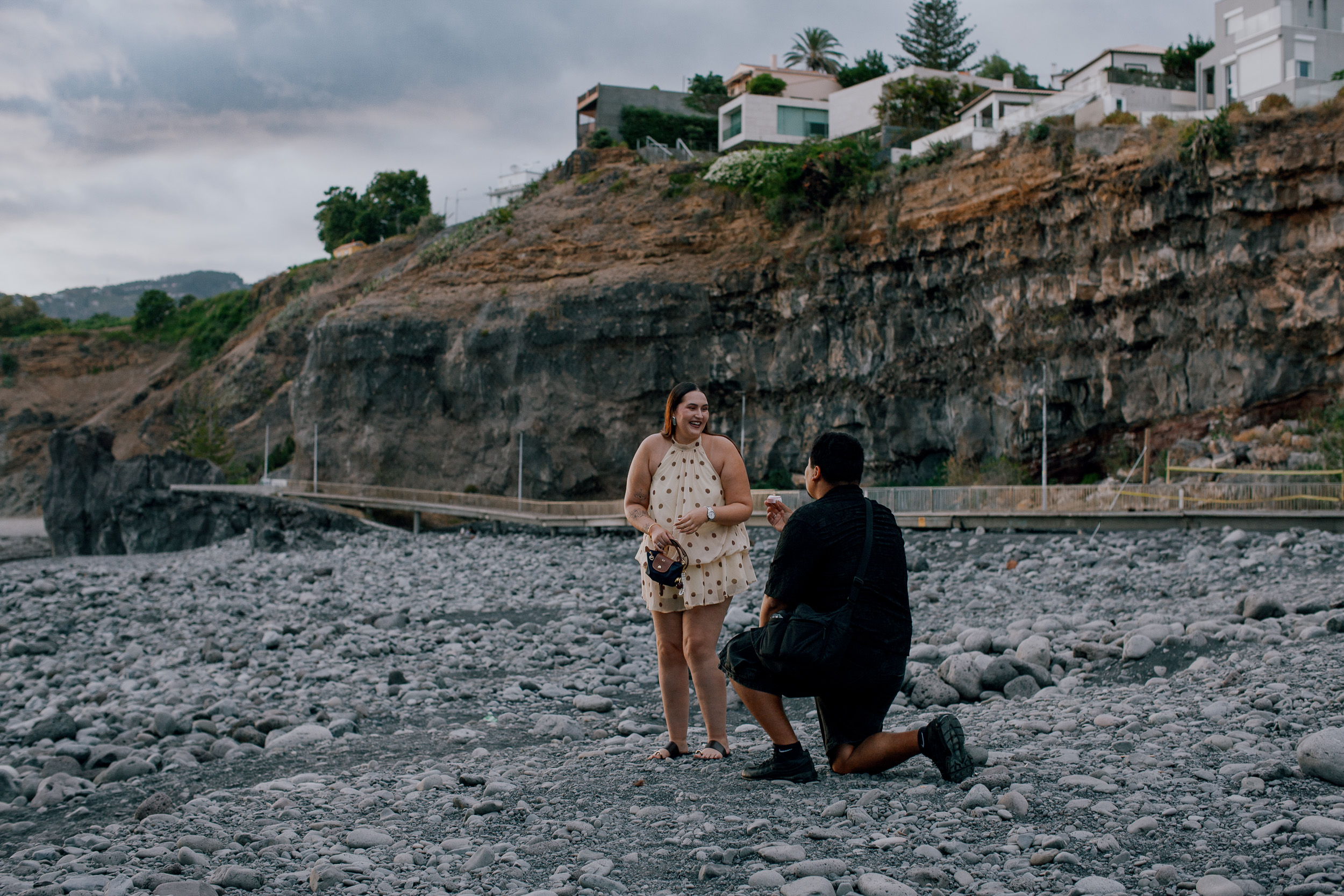 The proposal moment on the stony shore, houses on the cliff above, Praia Formosa, Madeira