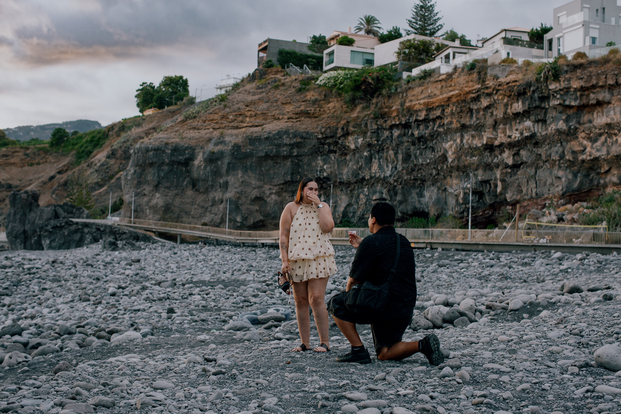 She covers her face as he kneels with the ring on the beach at Praia Formosa, Madeira