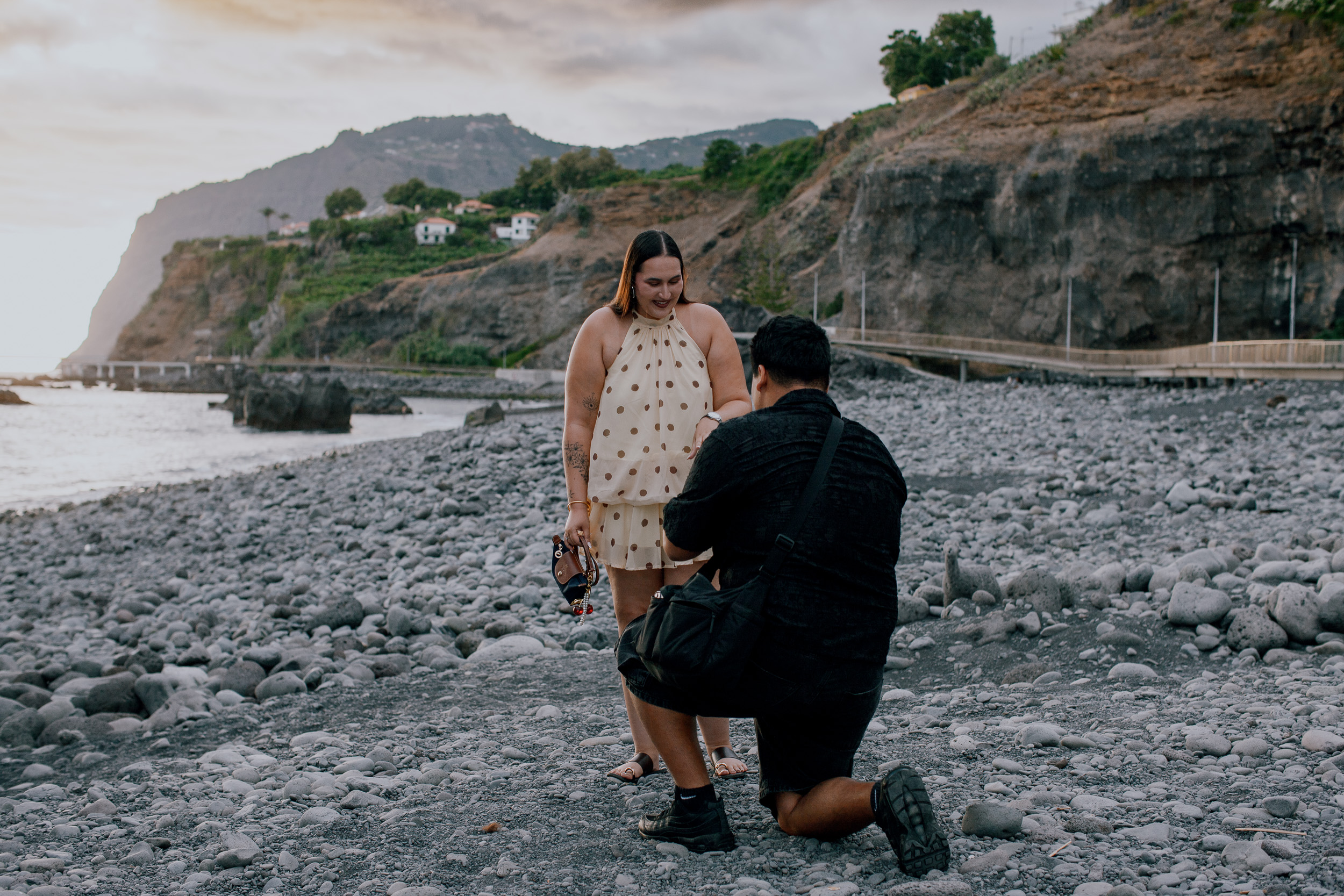 Saying yes on the pebbles with the old pier behind, surprise proposal at Praia Formosa, Madeira