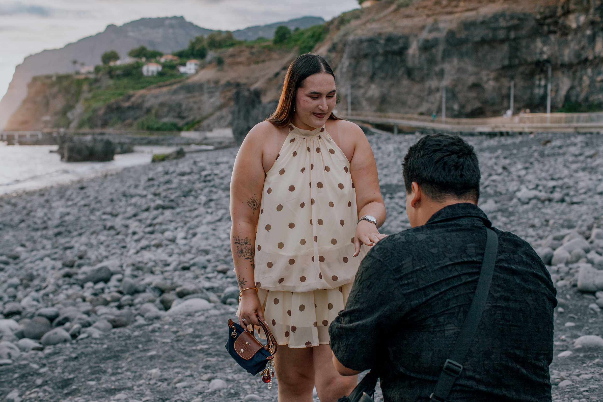 He stays on one knee holding the ring box as she reaches for him, Praia Formosa, Madeira