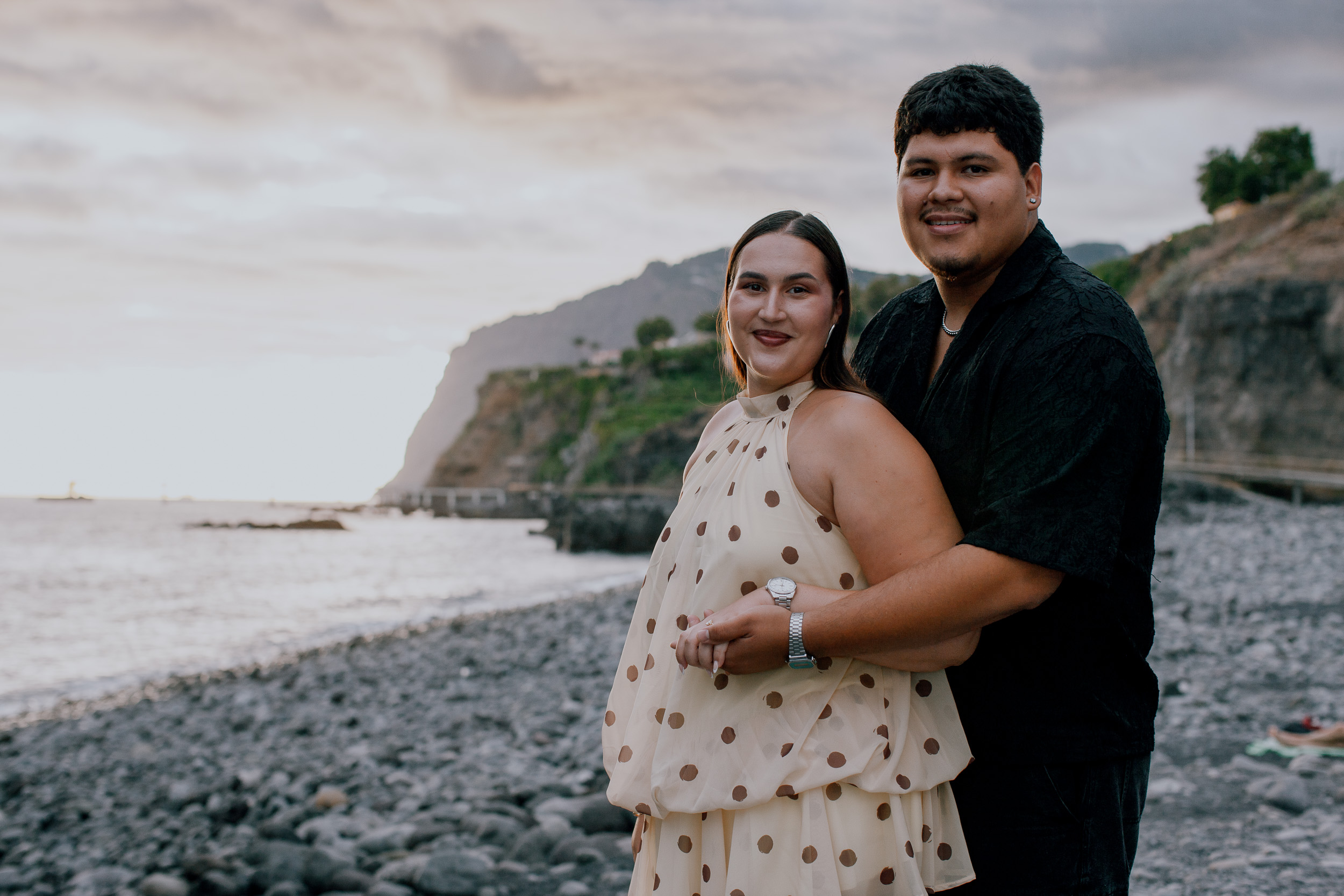 Newly engaged couple smiling on the shore with the western cliffs behind, Praia Formosa, Madeira
