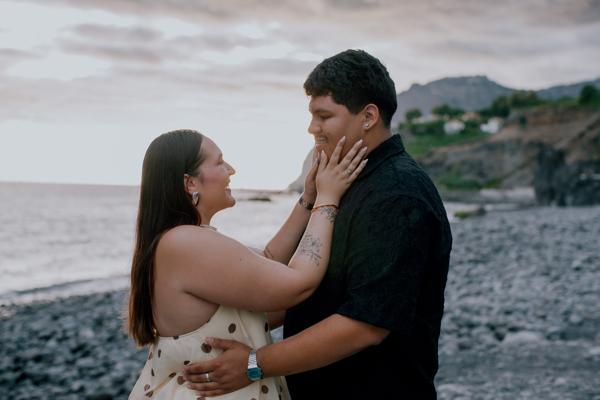 She holds his face on the pebble beach after saying yes, Praia Formosa, Madeira