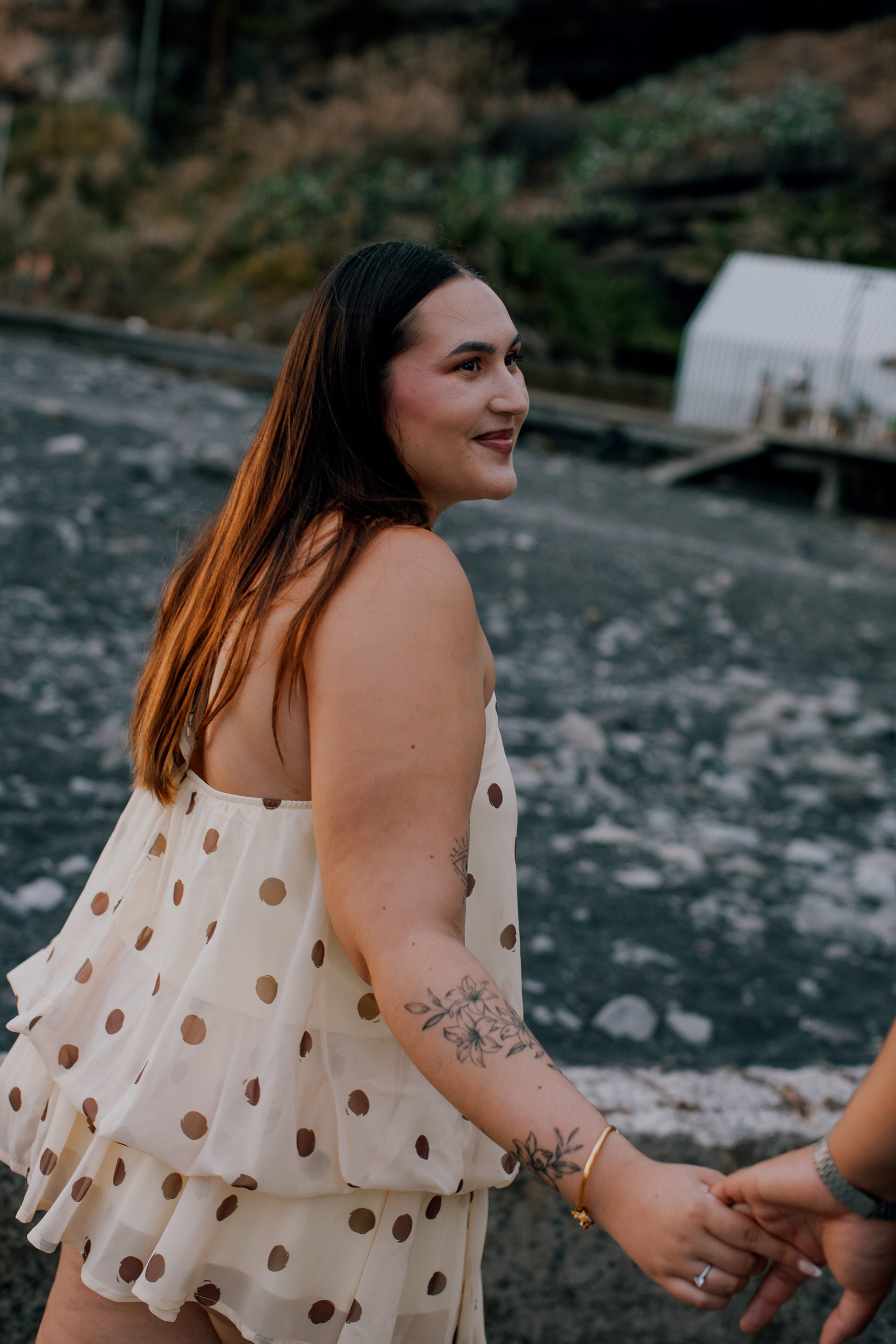 She leads him by the hand across the dark sand, engagement session at Praia Formosa, Madeira