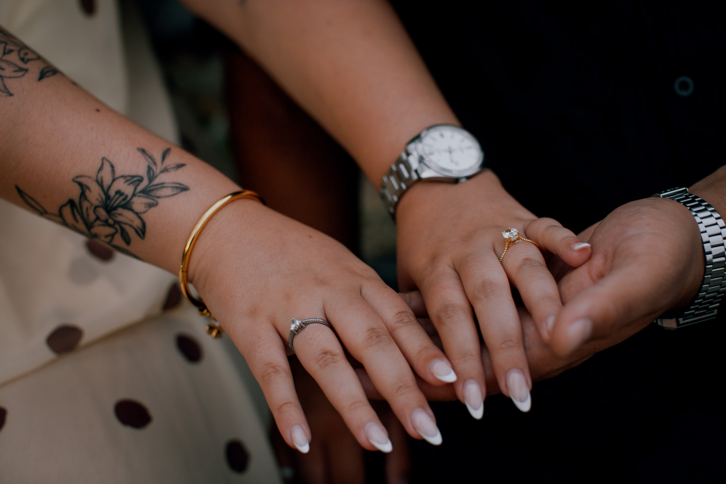 Engagement ring detail over her tattooed forearm and his watch, Praia Formosa, Madeira