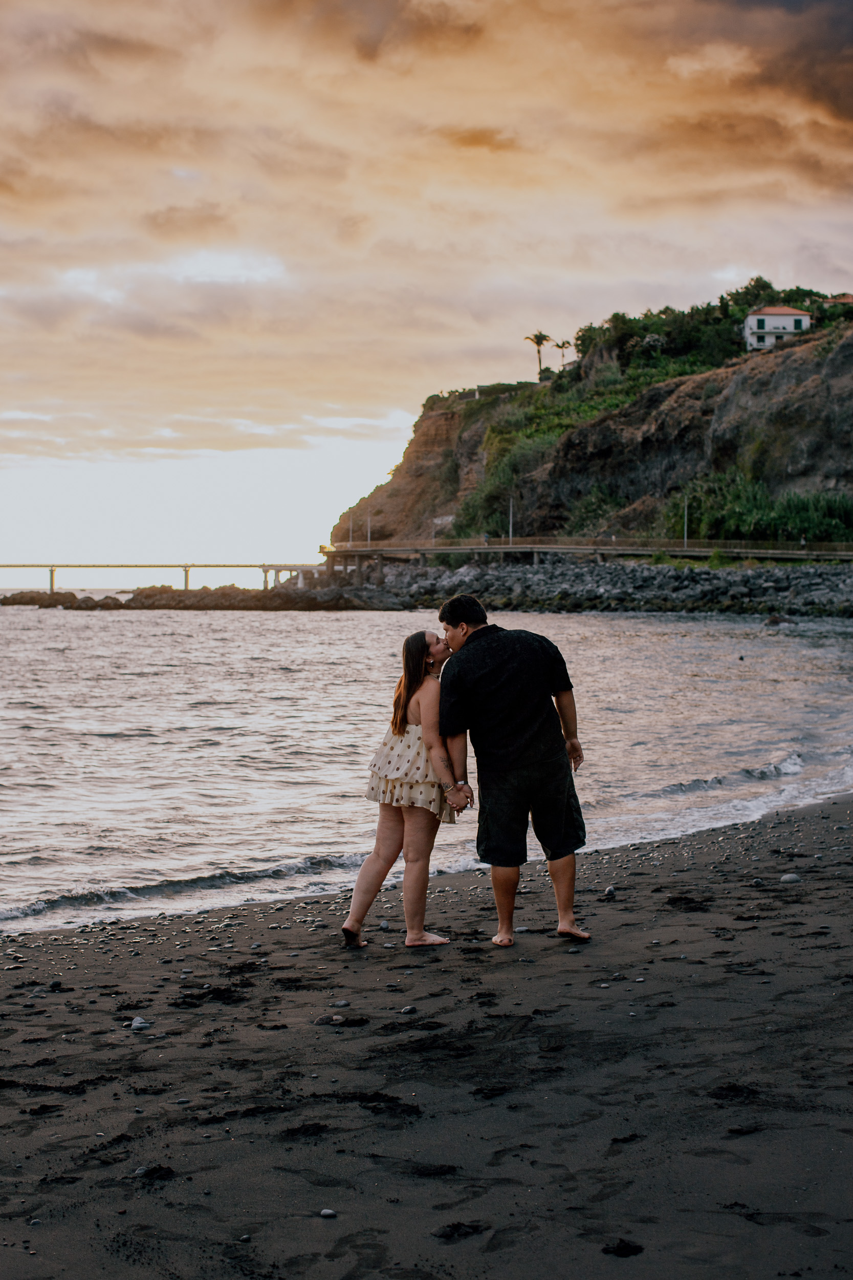 Kissing at the waterline under an orange sunset sky, engagement evening on Madeira
