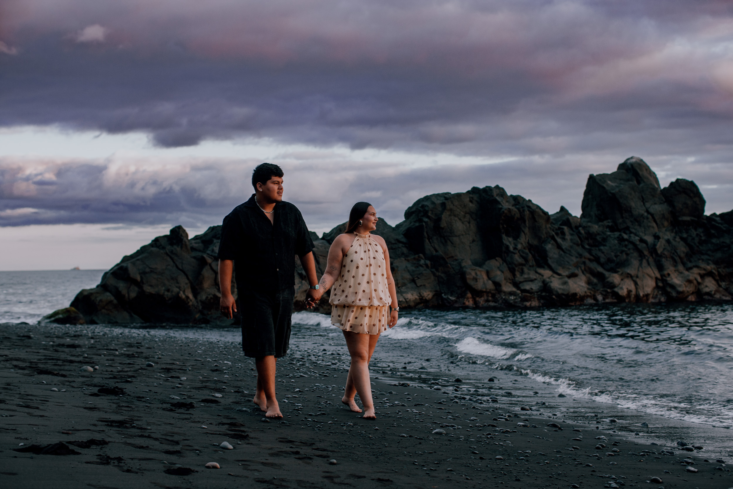 Walking hand in hand past the sea stack on the black sand, Praia Formosa, Madeira