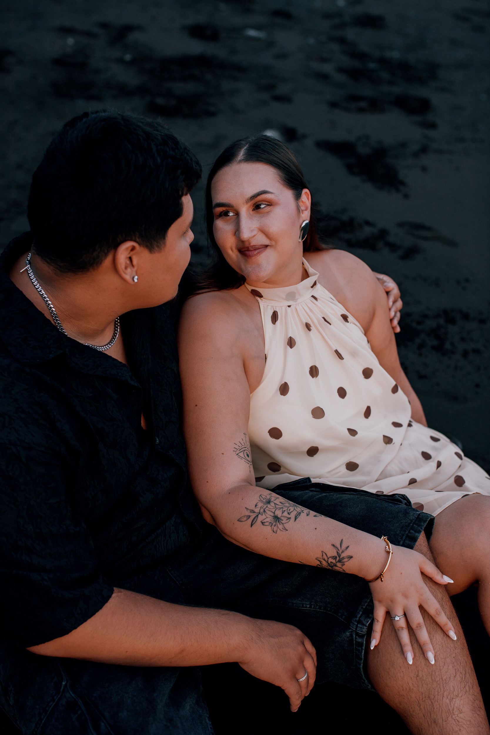 Sitting close together on the black sand, engagement session at Praia Formosa, Madeira