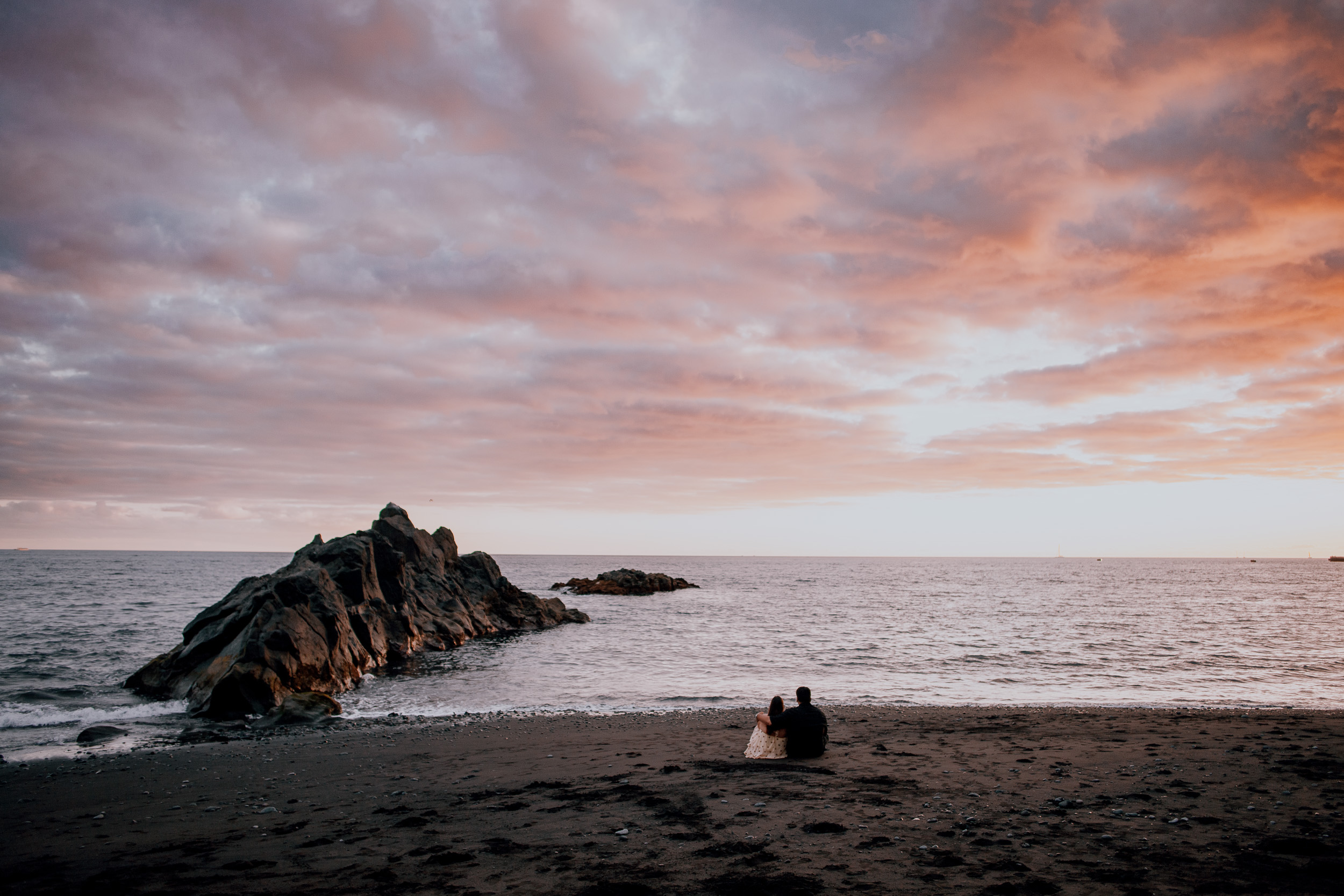 The couple tiny on the beach beneath a burning sunset sky, Praia Formosa, Madeira