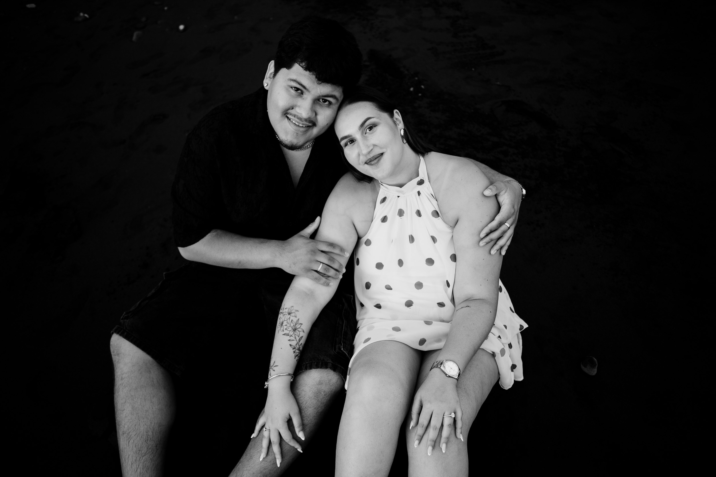 Black and white portrait seated on the dark sand, engaged couple on Madeira