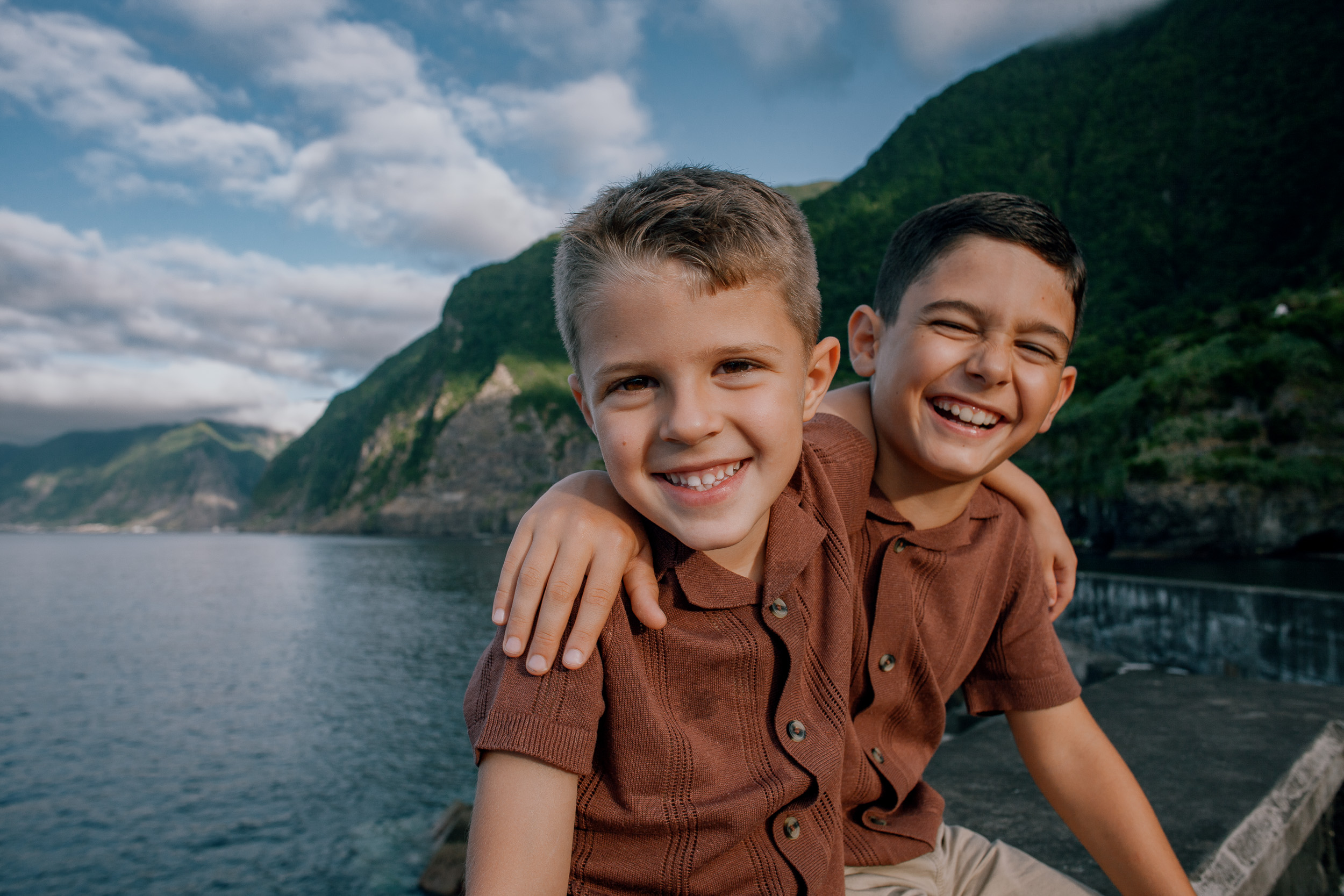 Brothers arm in arm grinning on the seawall, green cliffs behind, Seixal, Madeira