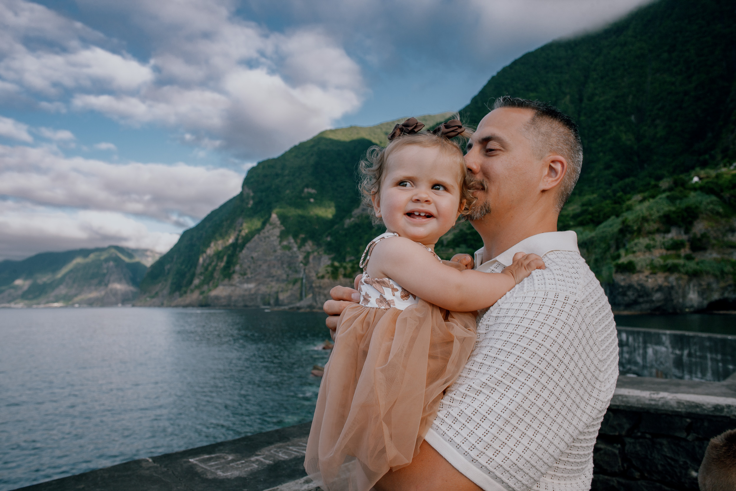 The baby girl beaming as her father kisses her cheek, cliffs behind, Seixal, Madeira
