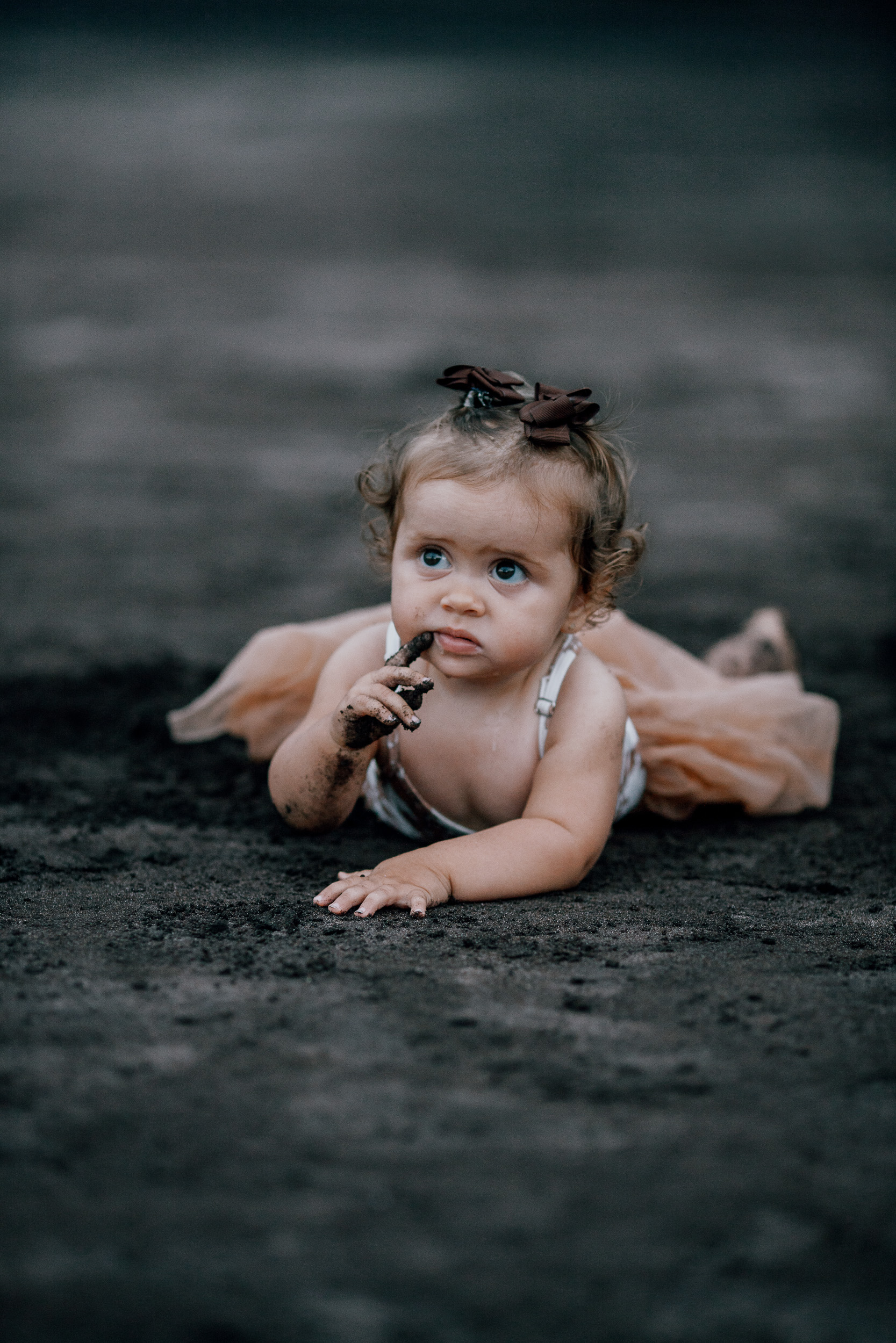 The baby girl lying on the sand chewing her bow, Seixal Beach, Madeira