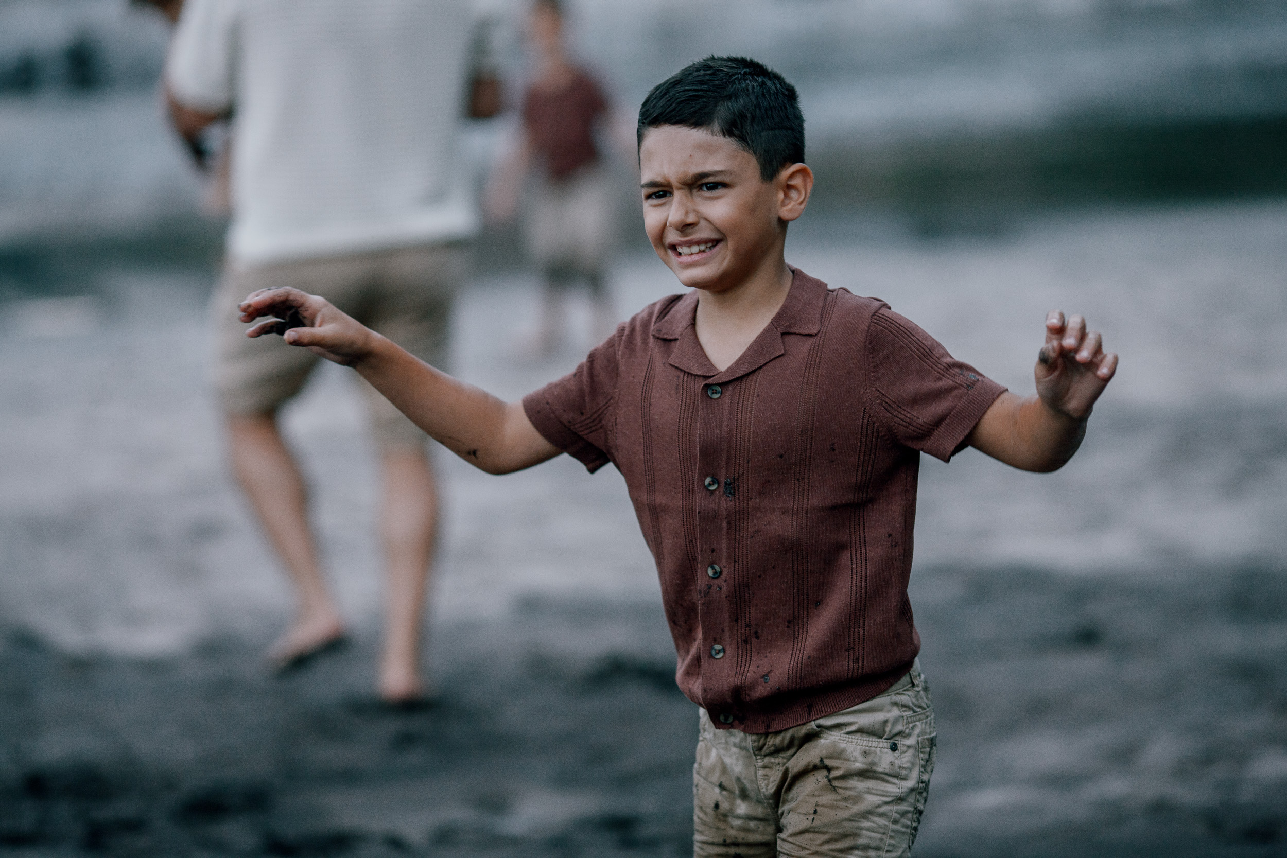 The younger boy charging across the beach grinning, dad behind, Seixal, Madeira