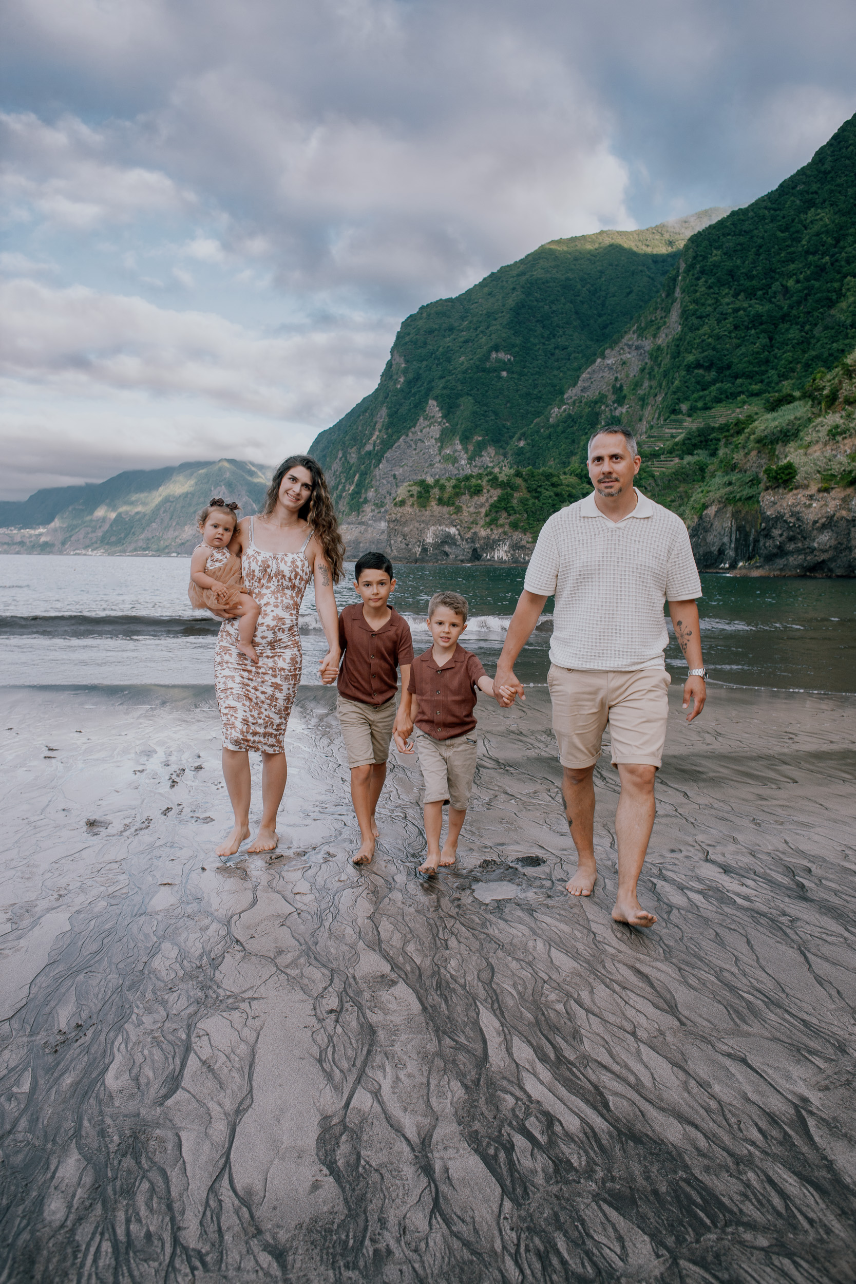 The family walking the black sand, cliffs sunlit behind, Seixal, Madeira