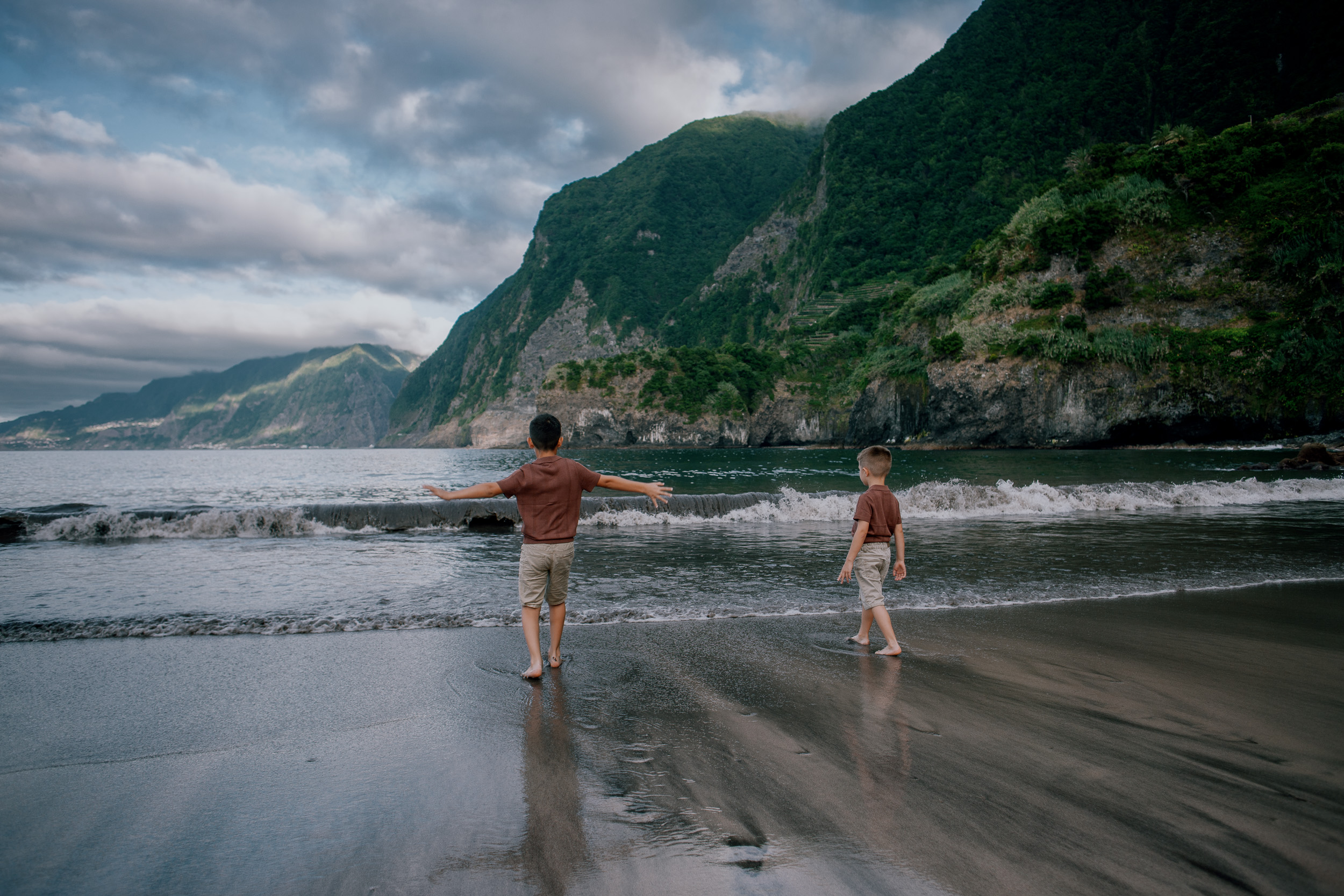 The boys running into the surf on the dark sand, Seixal Beach, Madeira