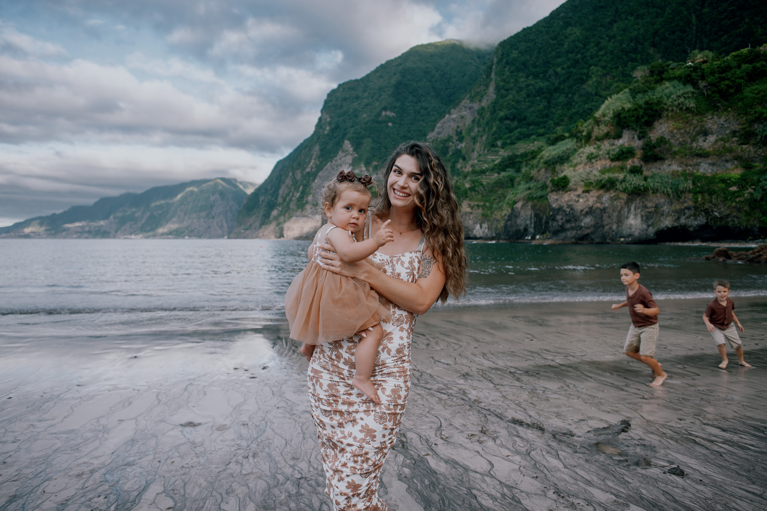 Mother holding the baby girl as the boys play behind, Seixal Beach, Madeira