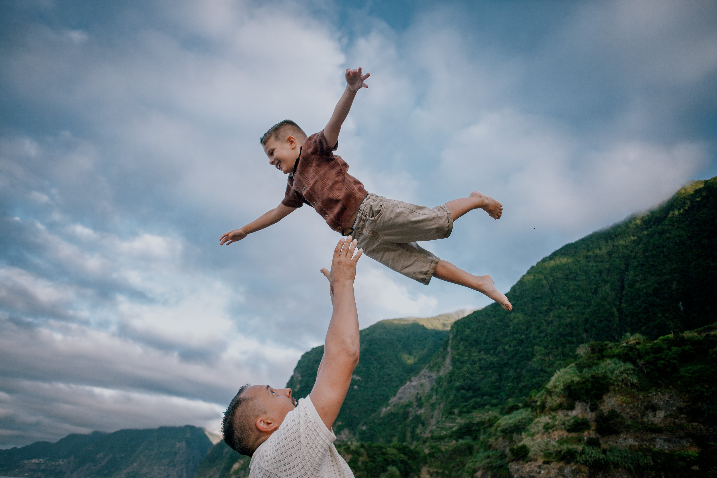 Son mid-air in a star shape over dad's head, sky behind, Seixal Beach, Madeira