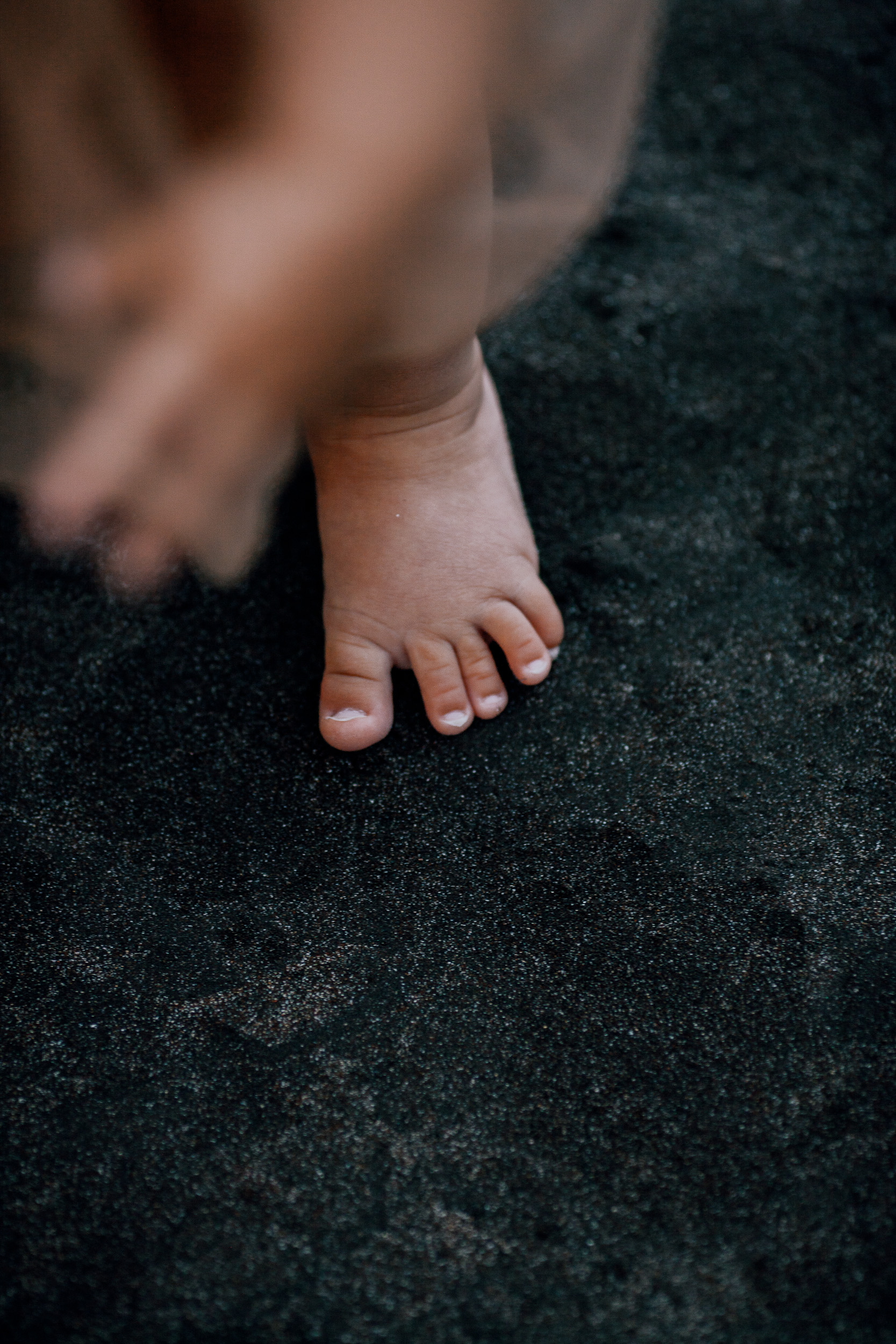 The baby's bare foot on the black sand, close detail, Seixal Beach, Madeira