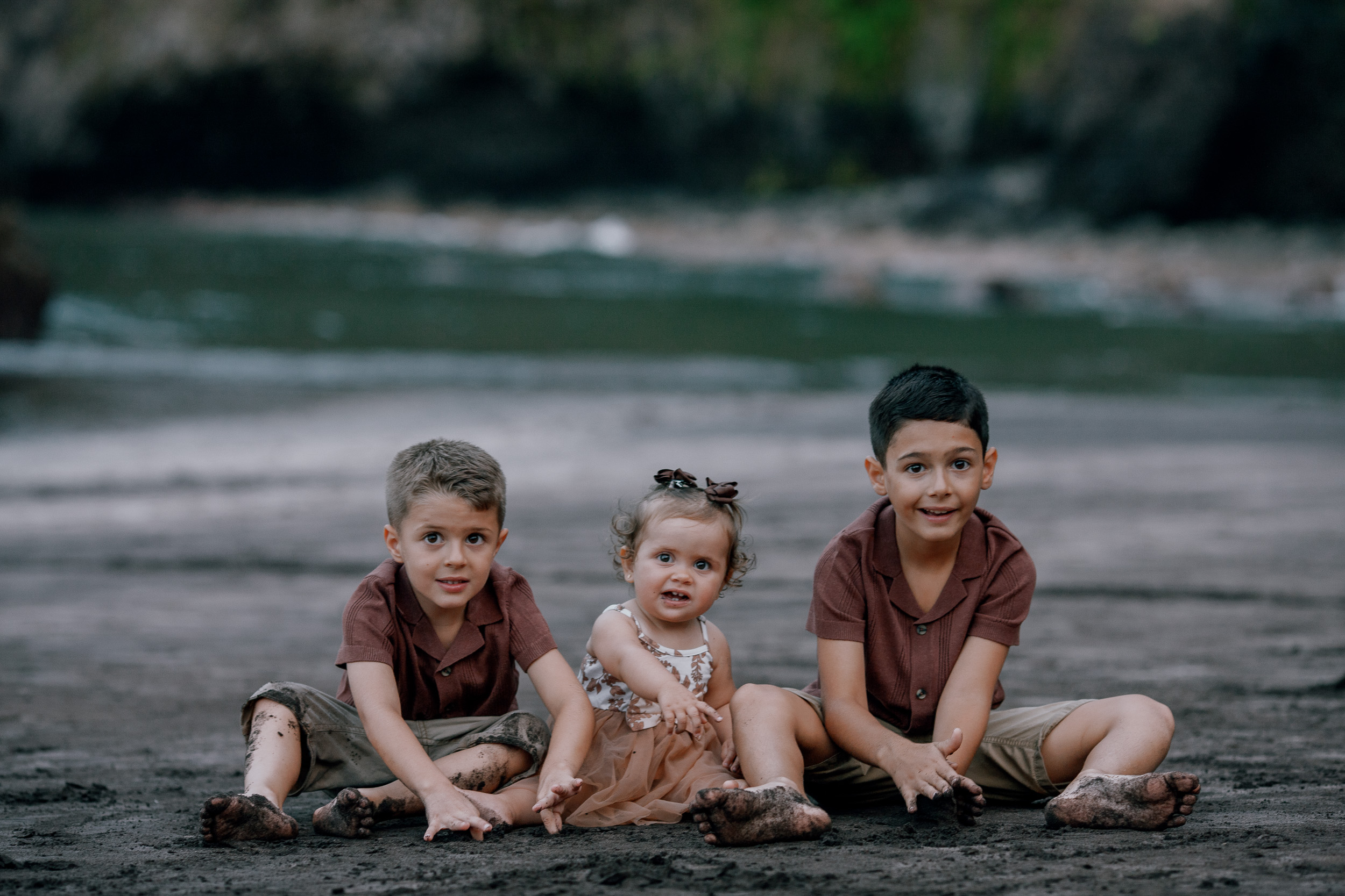 The three kids sitting together on the dark sand, Seixal Beach, Madeira