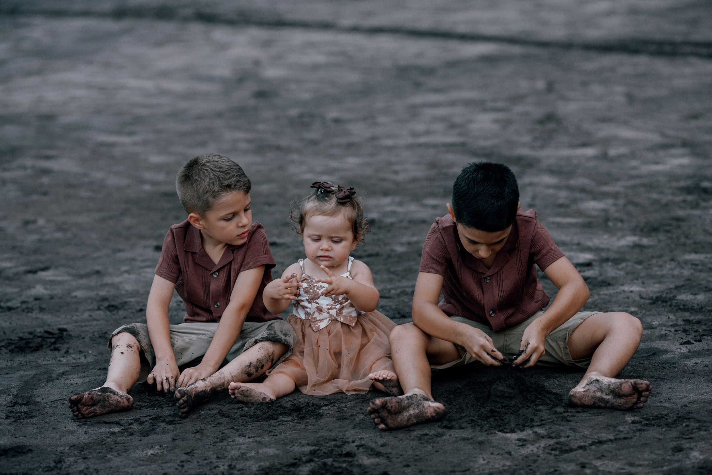 Brothers and baby sister sitting in a row on the beach, Seixal, Madeira