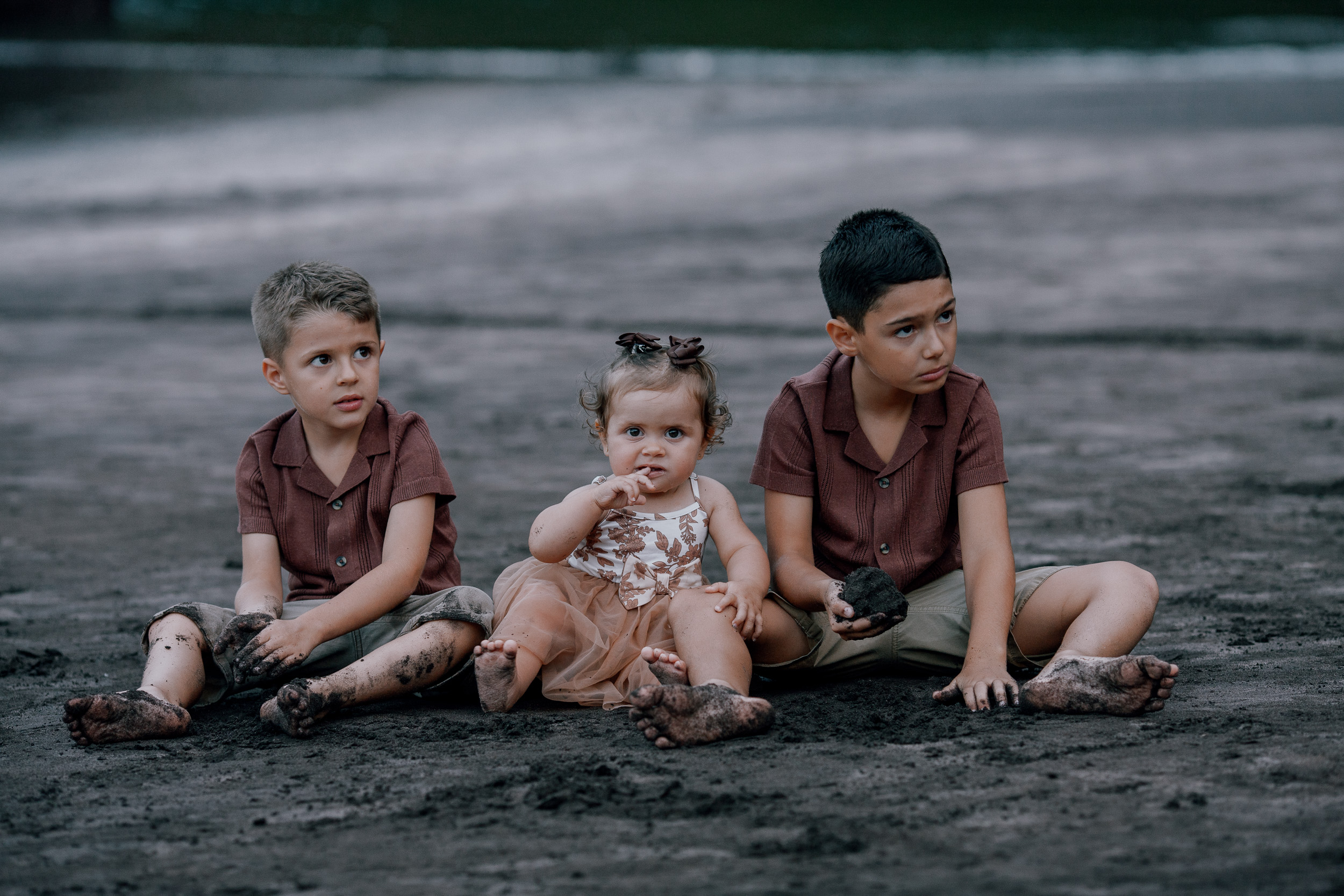 Three children side by side on the black sand, sky heavy above, Seixal, Madeira