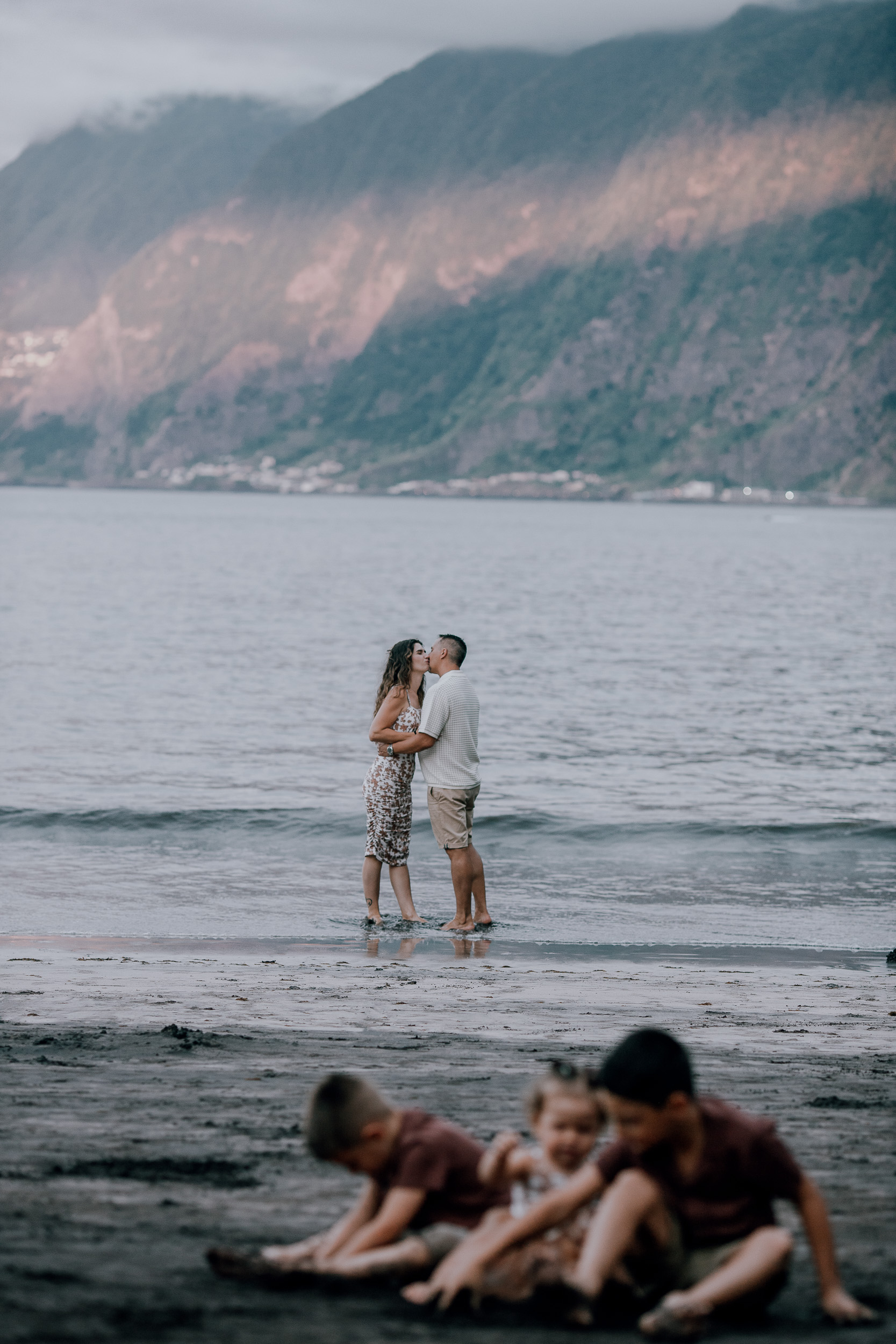 Parents kissing behind the kids playing on the sand, Seixal, Madeira