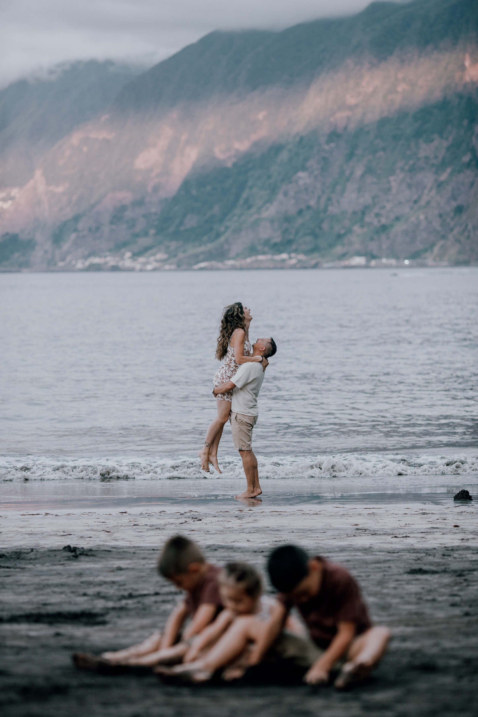 Dad lifting mum off her feet as the kids dig behind, Seixal Beach, Madeira