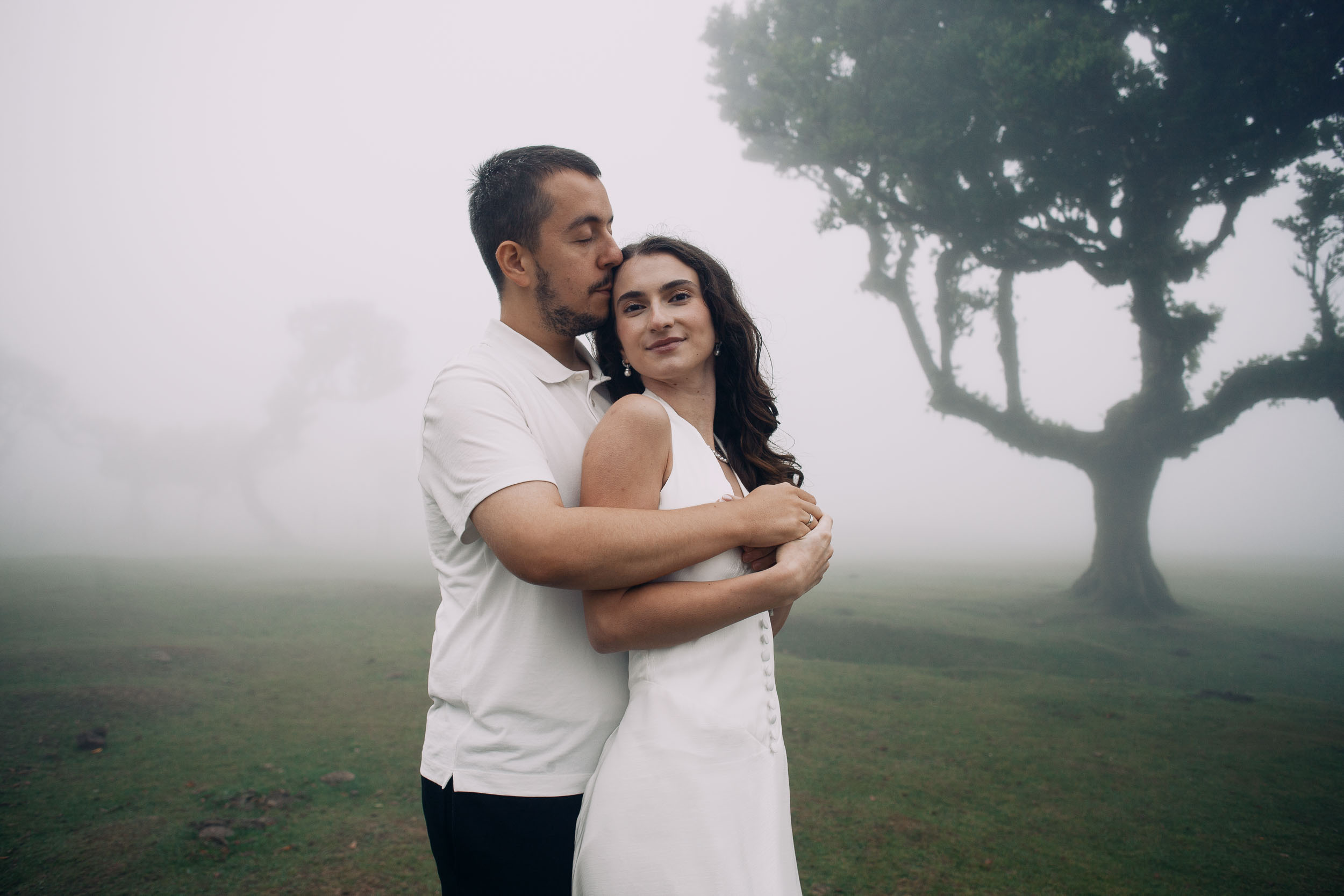 Man holding his wife from behind and kissing her temple among the laurels of Fanal Forest, Madeira