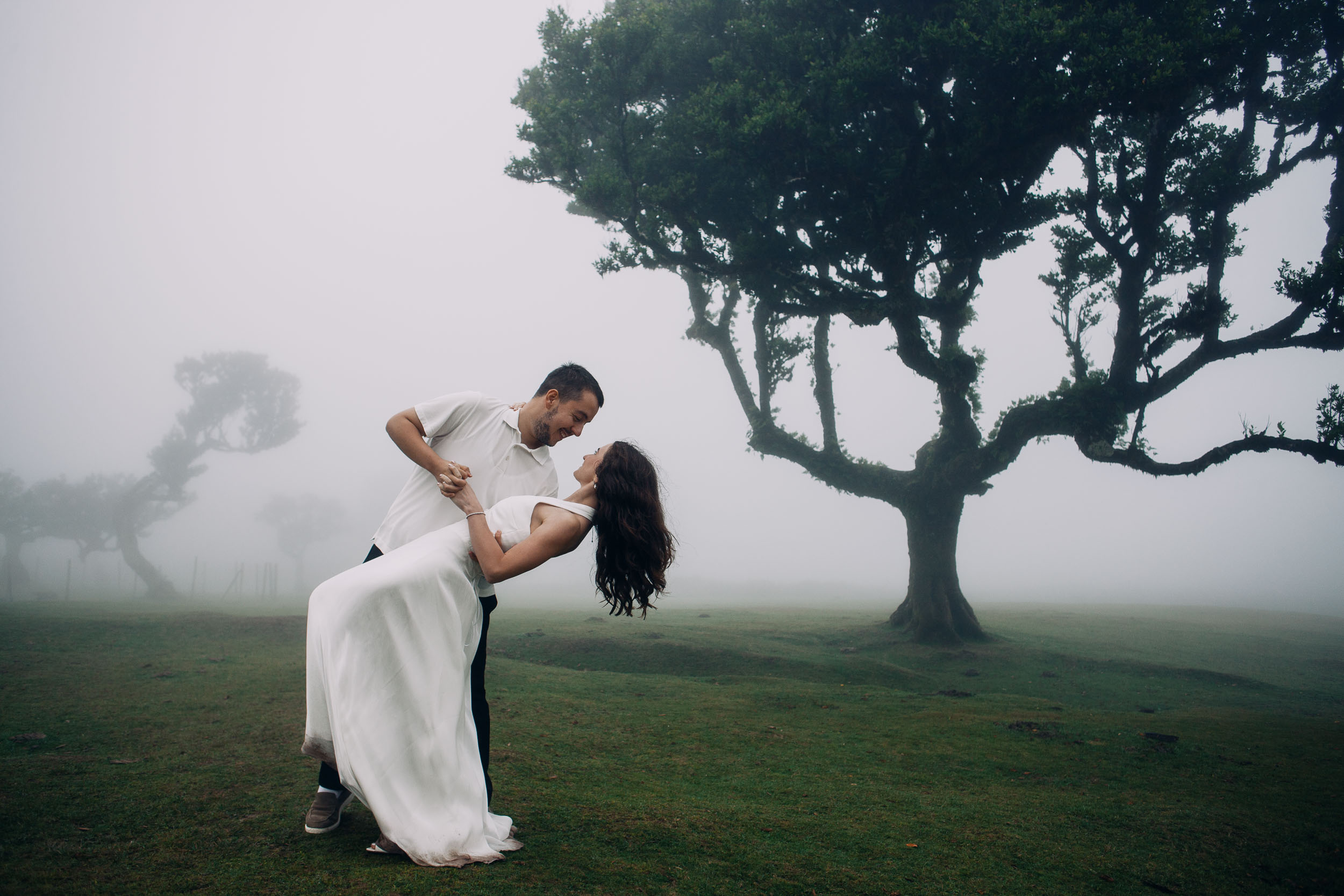 Man leaning his wife back in a dance hold, both laughing, ancient laurel behind, Fanal Forest, Madeira