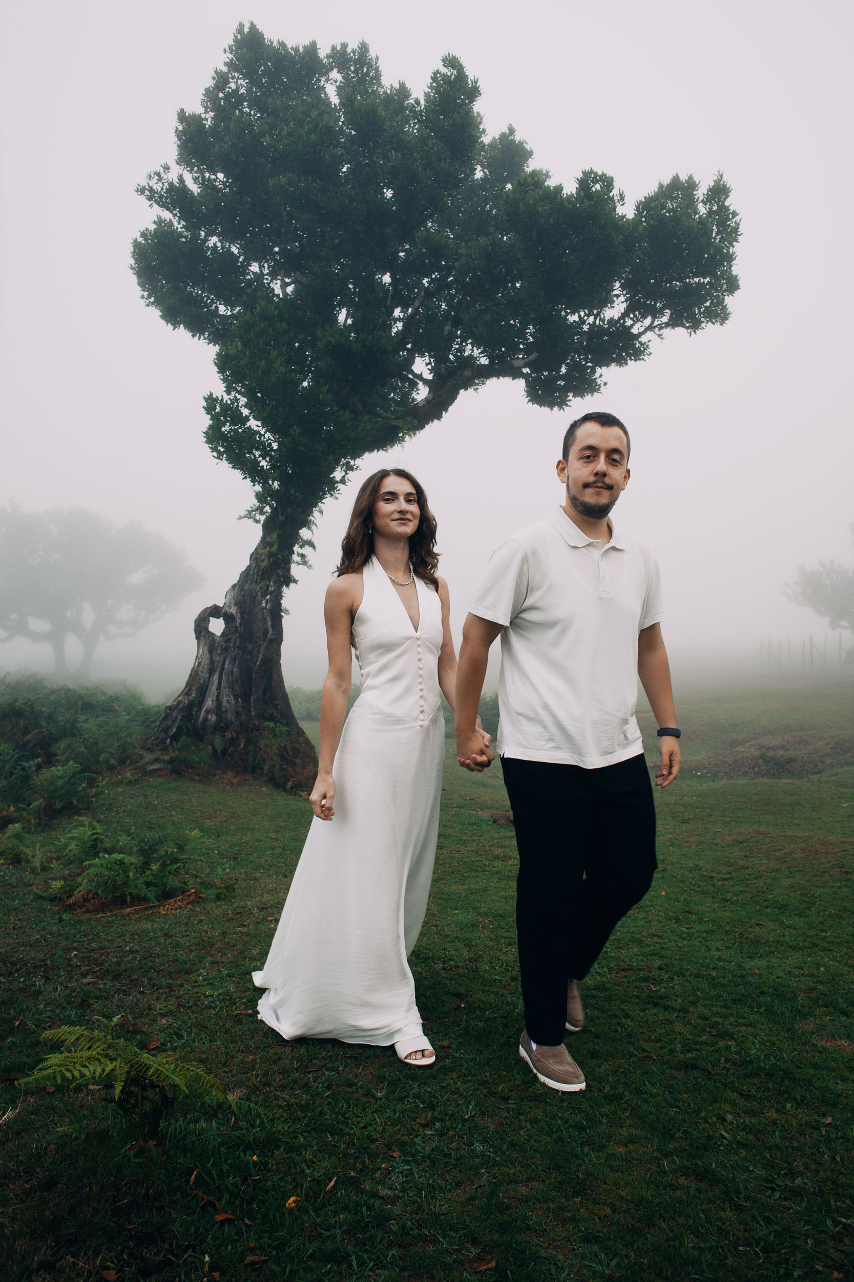 Couple walking toward the camera hand in hand under a laurel canopy, Fanal Forest, Madeira