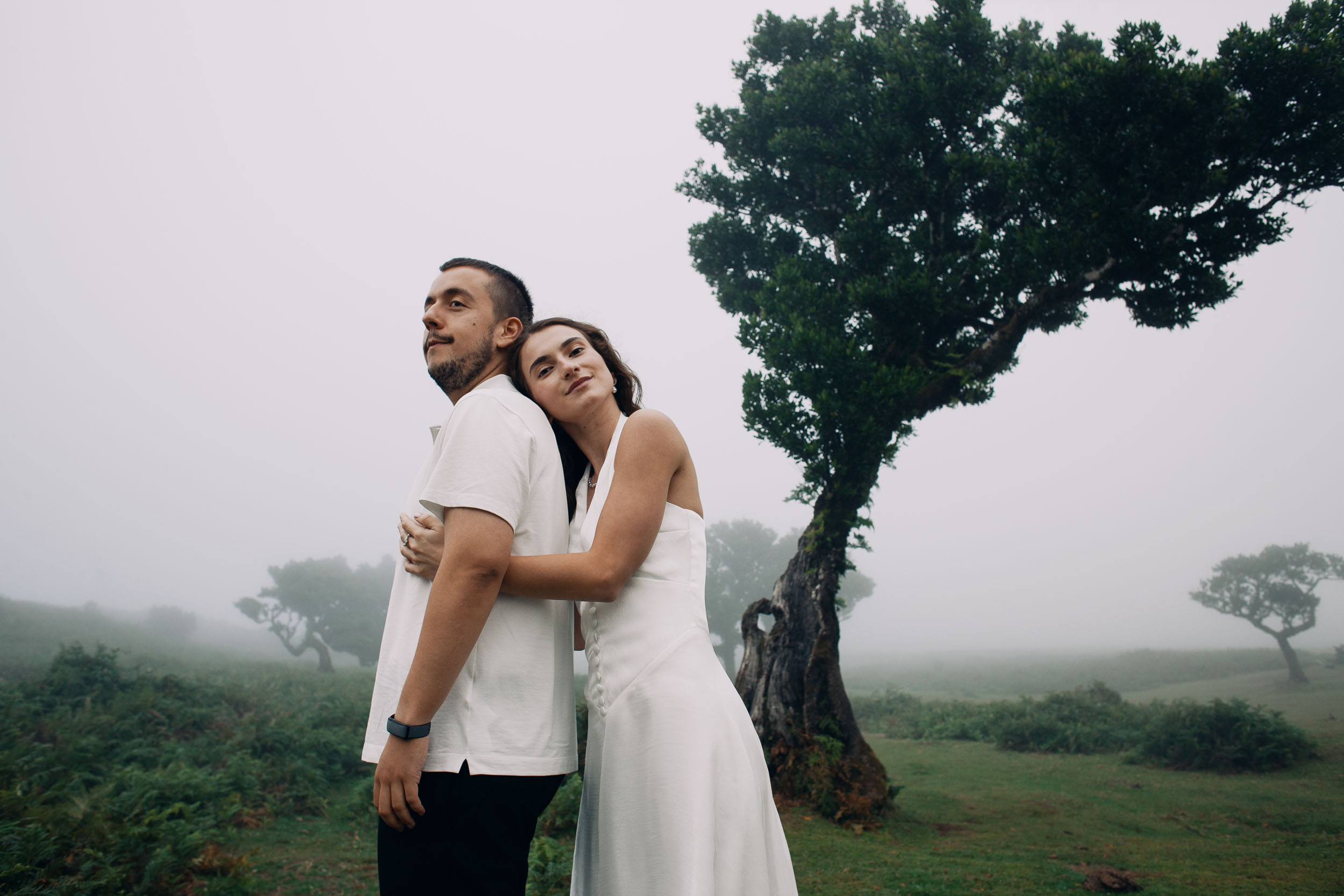 She leans on his back with her arms around him, laurel trunk beside them, Fanal Forest, Madeira