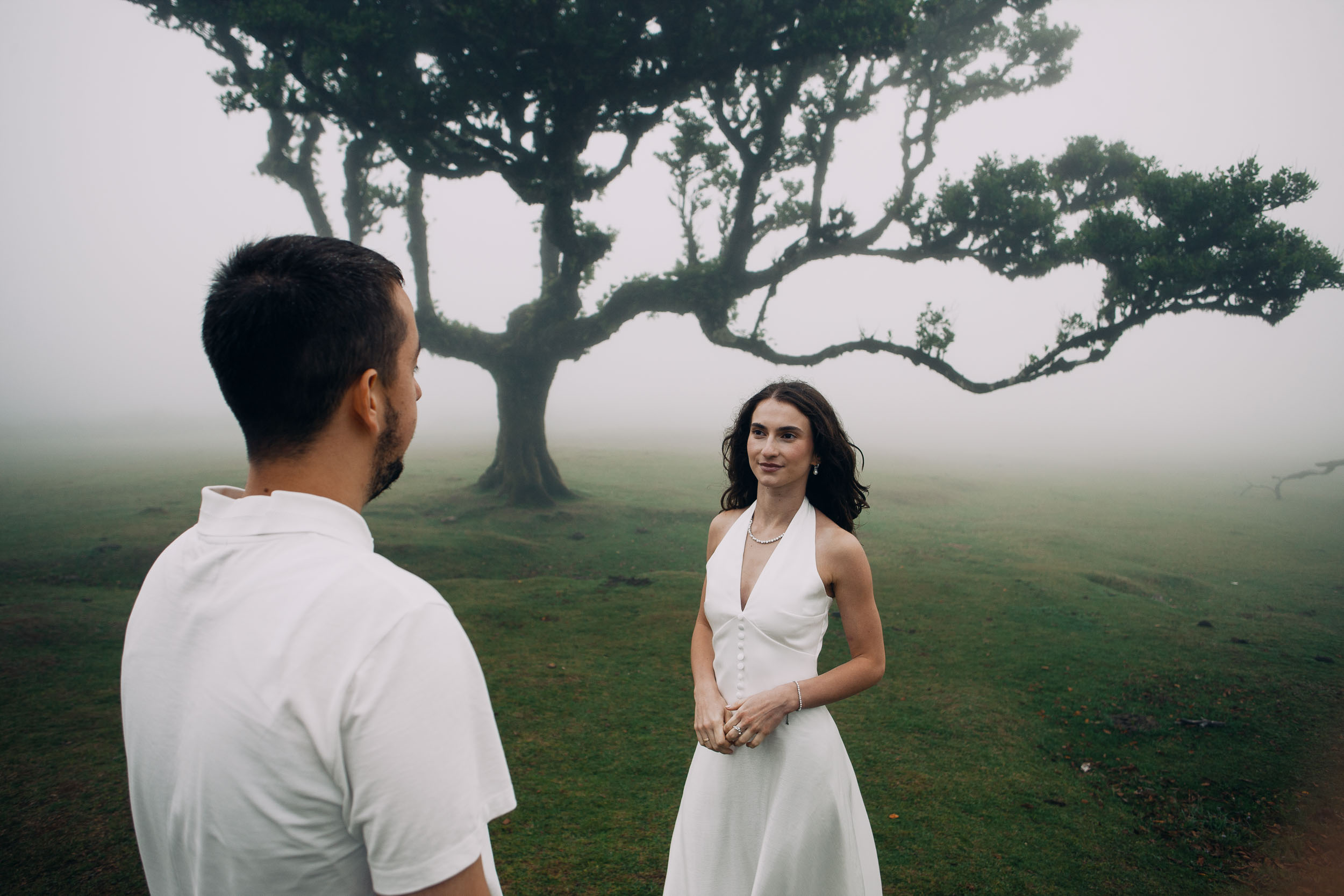 Close frame over his shoulder, she faces him in front of a wide laurel, Fanal Forest, Madeira