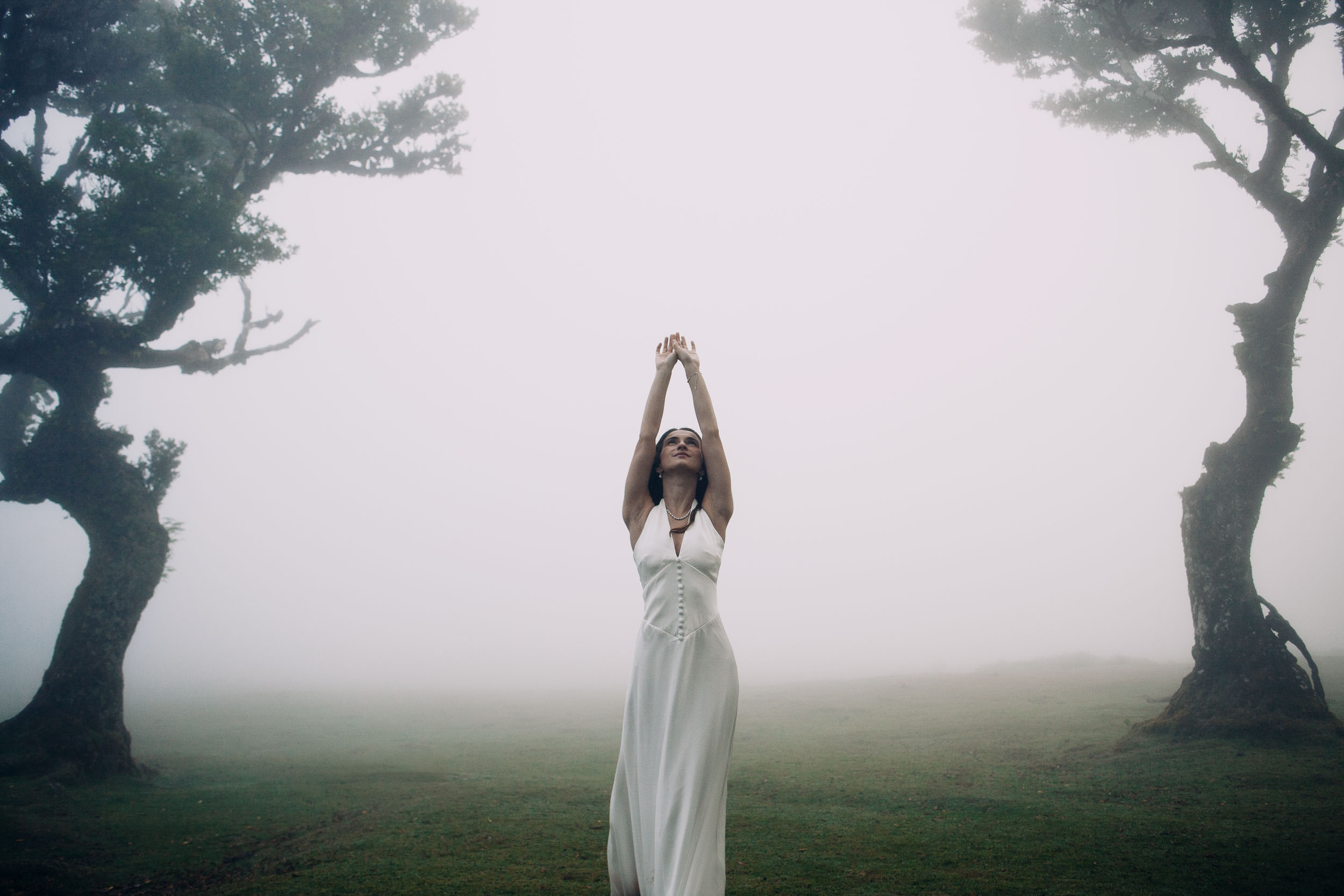 She raises her arms with fog closing in on both sides, Fanal Forest, Madeira