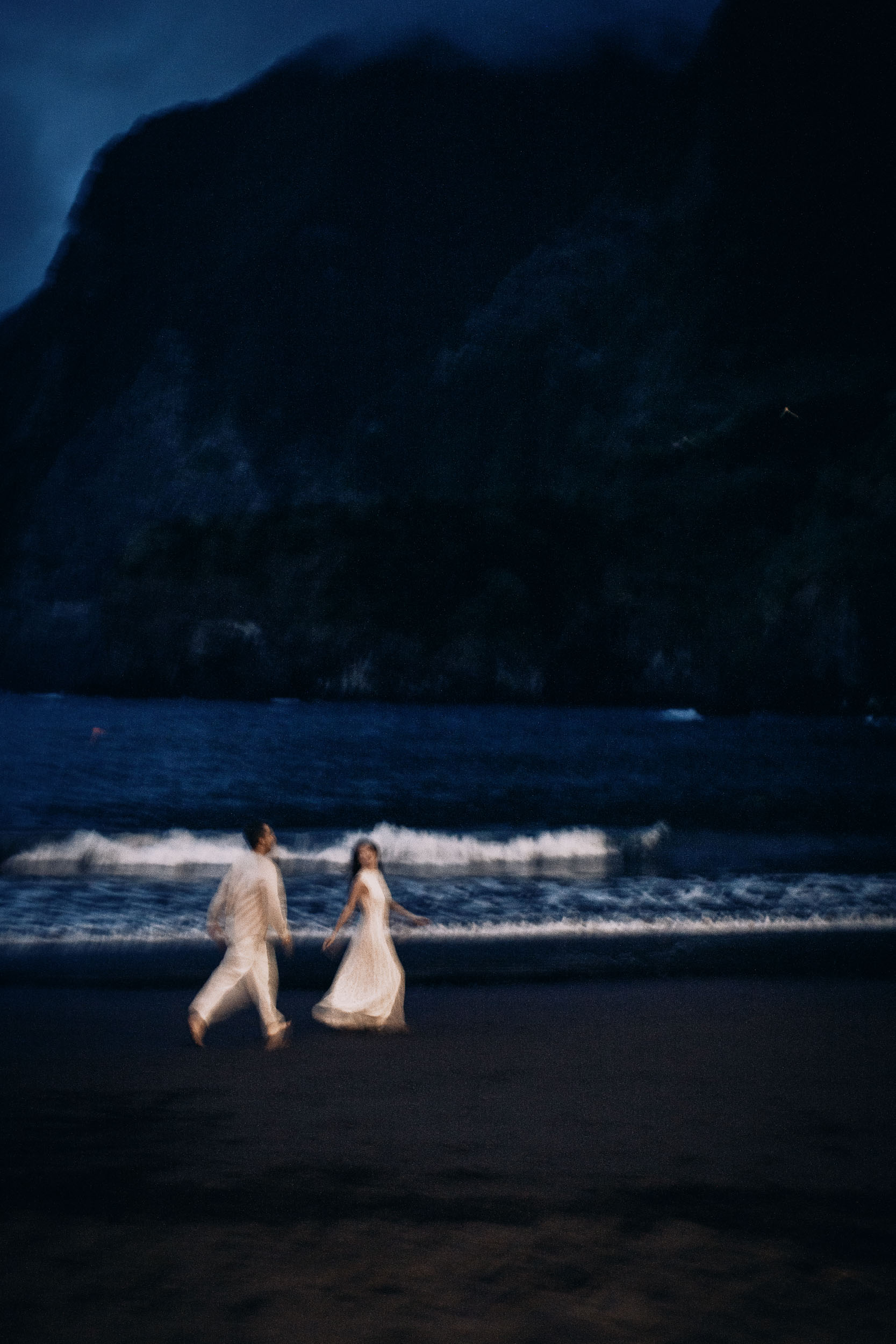 Couple walking barefoot through the surf under the dark cliff, Seixal Beach, Madeira