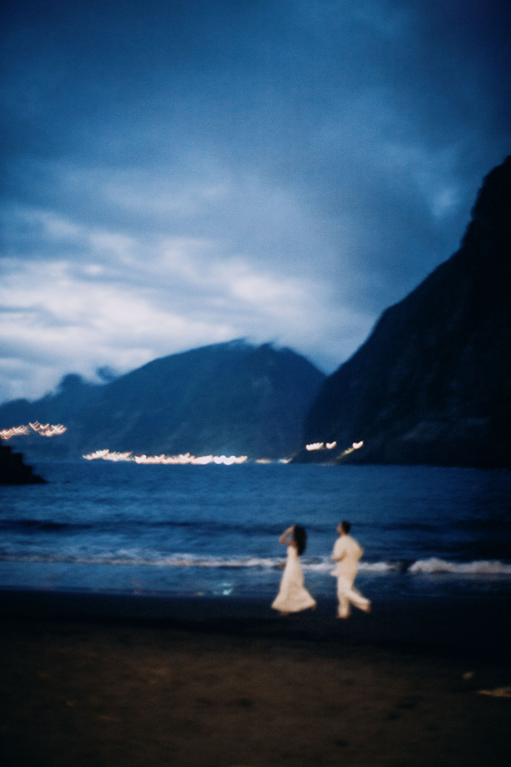 Couple at the waterline with the lights of the coast behind them, Seixal Beach, Madeira