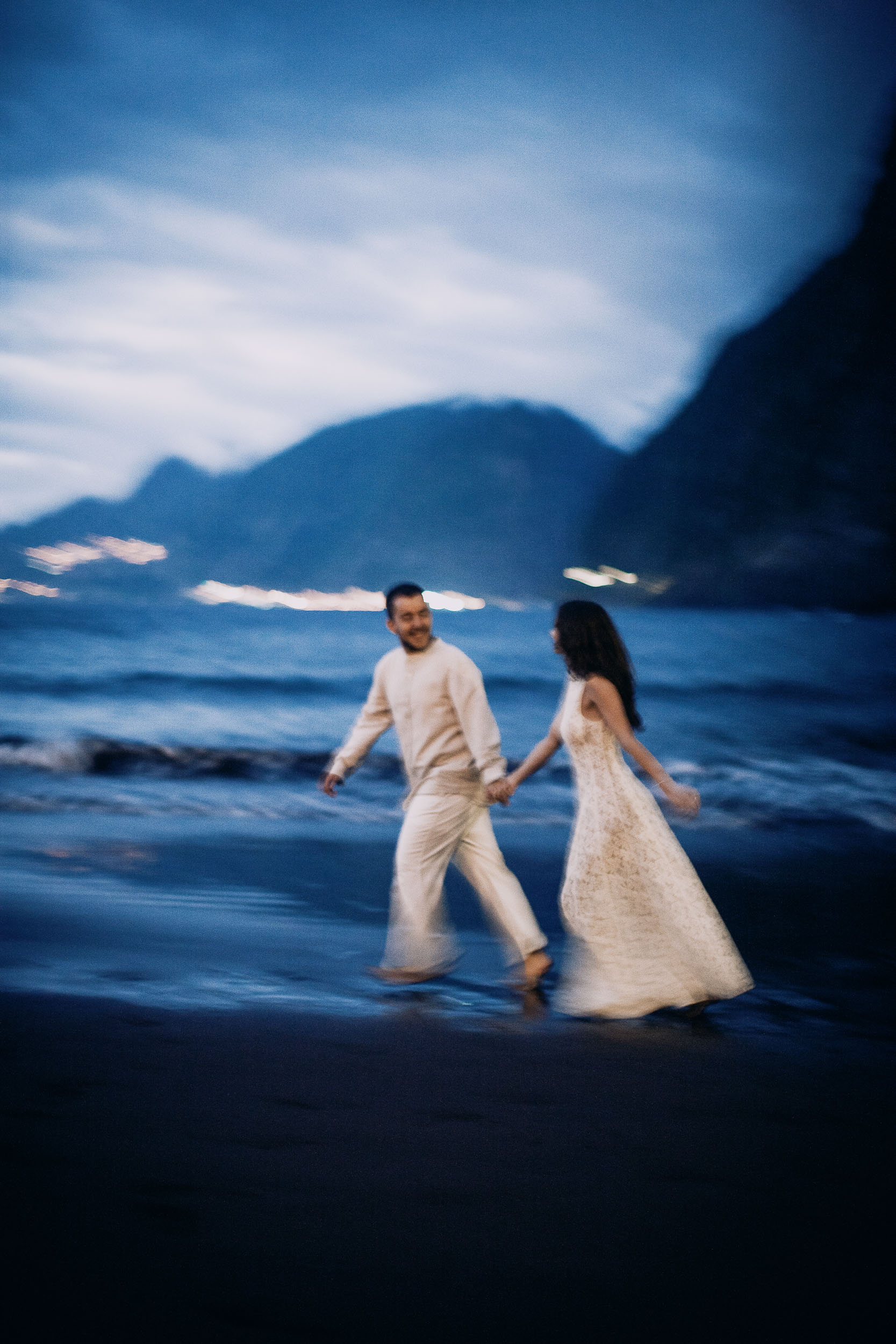 Couple crossing the shallows at blue hour, the far cliffs already dark, Seixal Beach, Madeira