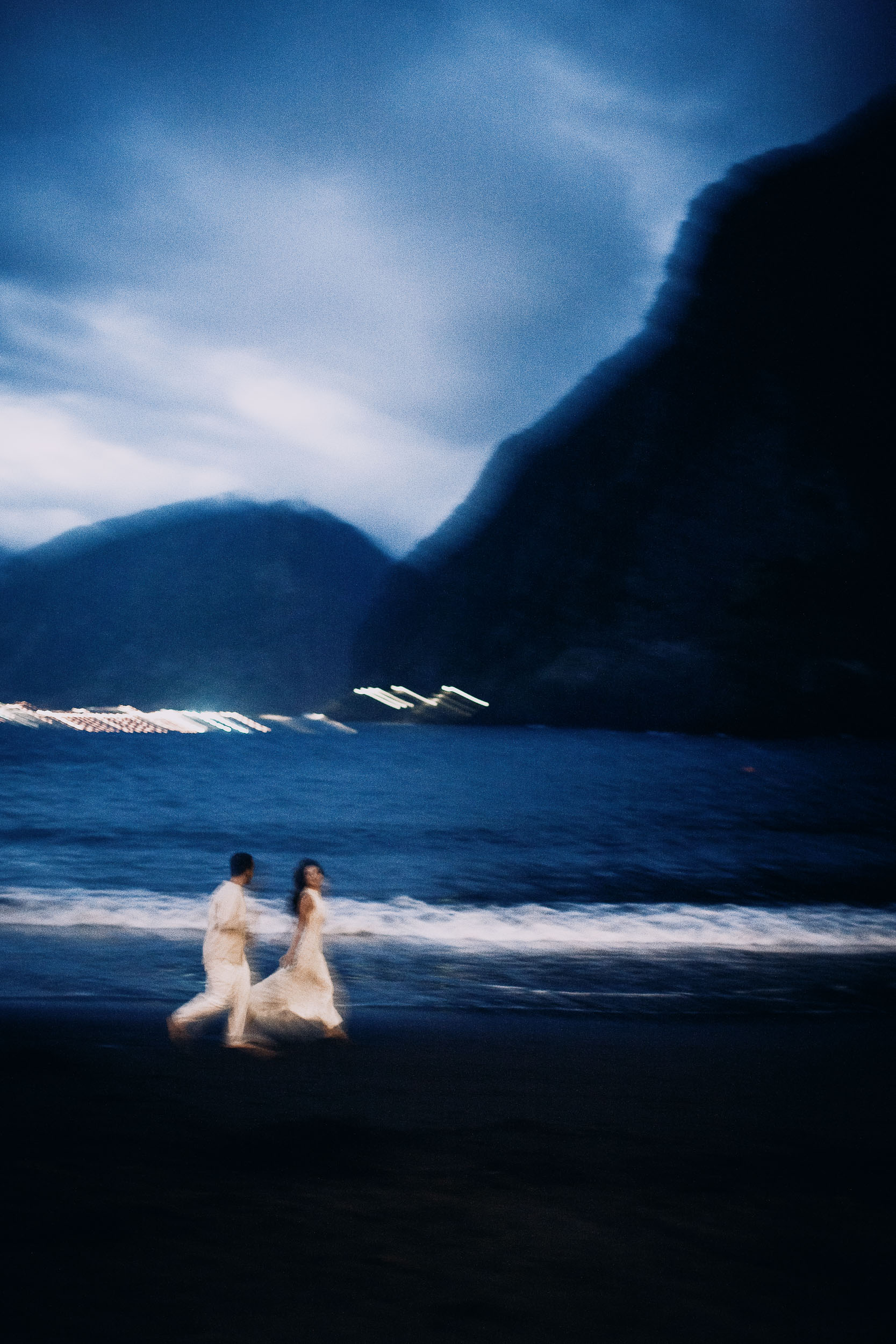 Couple walking along the base of the cliff on wet black sand, Seixal Beach, Madeira